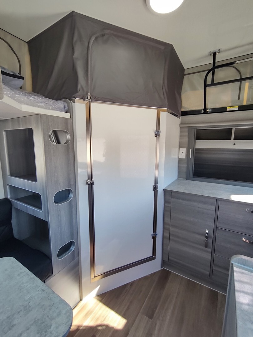 Inside a modern RV rental: view of bunk beds, pop-top sleeping area, and compact interior amenities.. OBI DWELLER 15' 2022