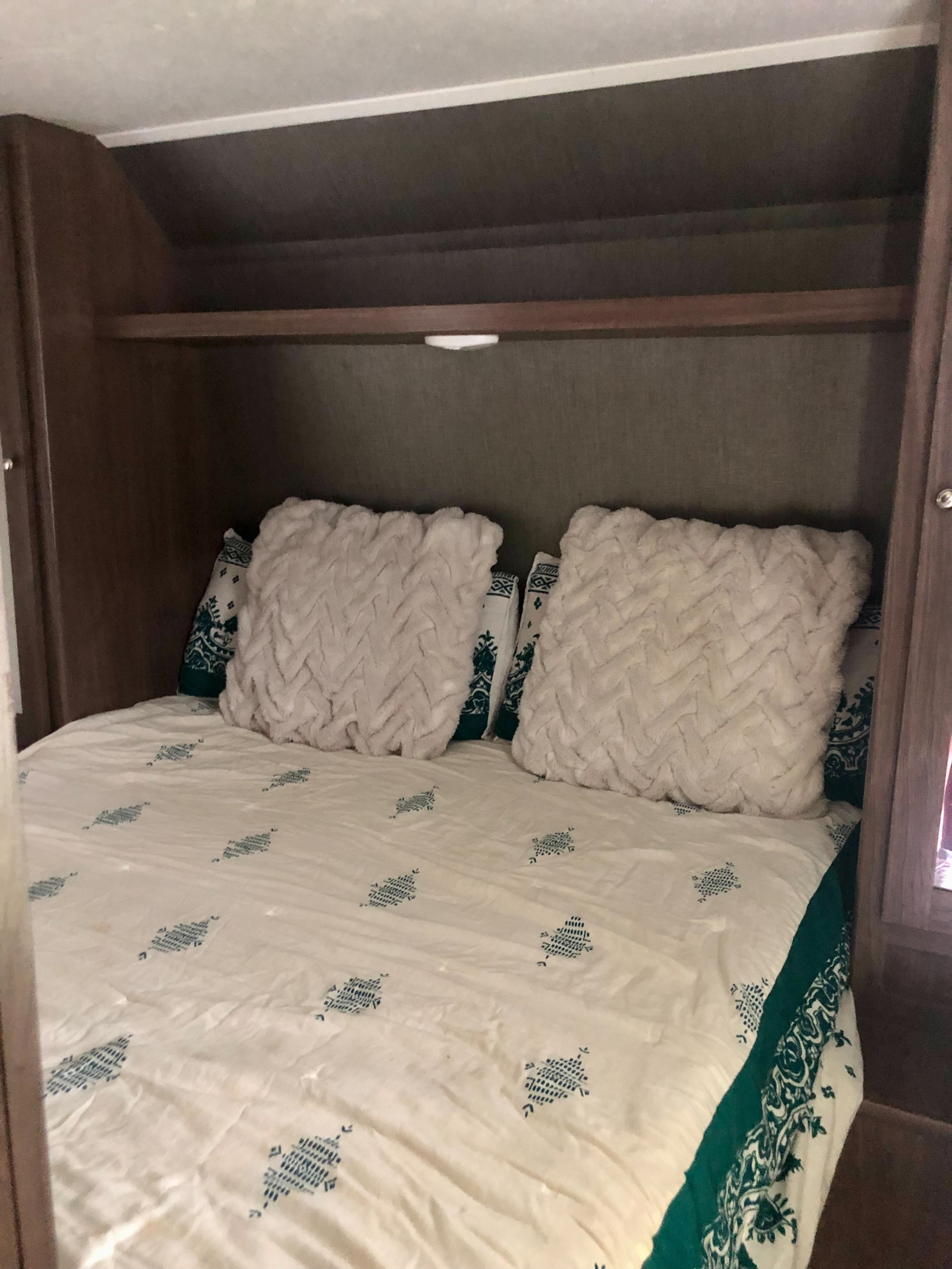 Inside an RV rental: a comfortable bedroom featuring a bed with patterned white & teal bedding, fluffy pillows, and overhead storage.. Keystone RV Hideout 2019