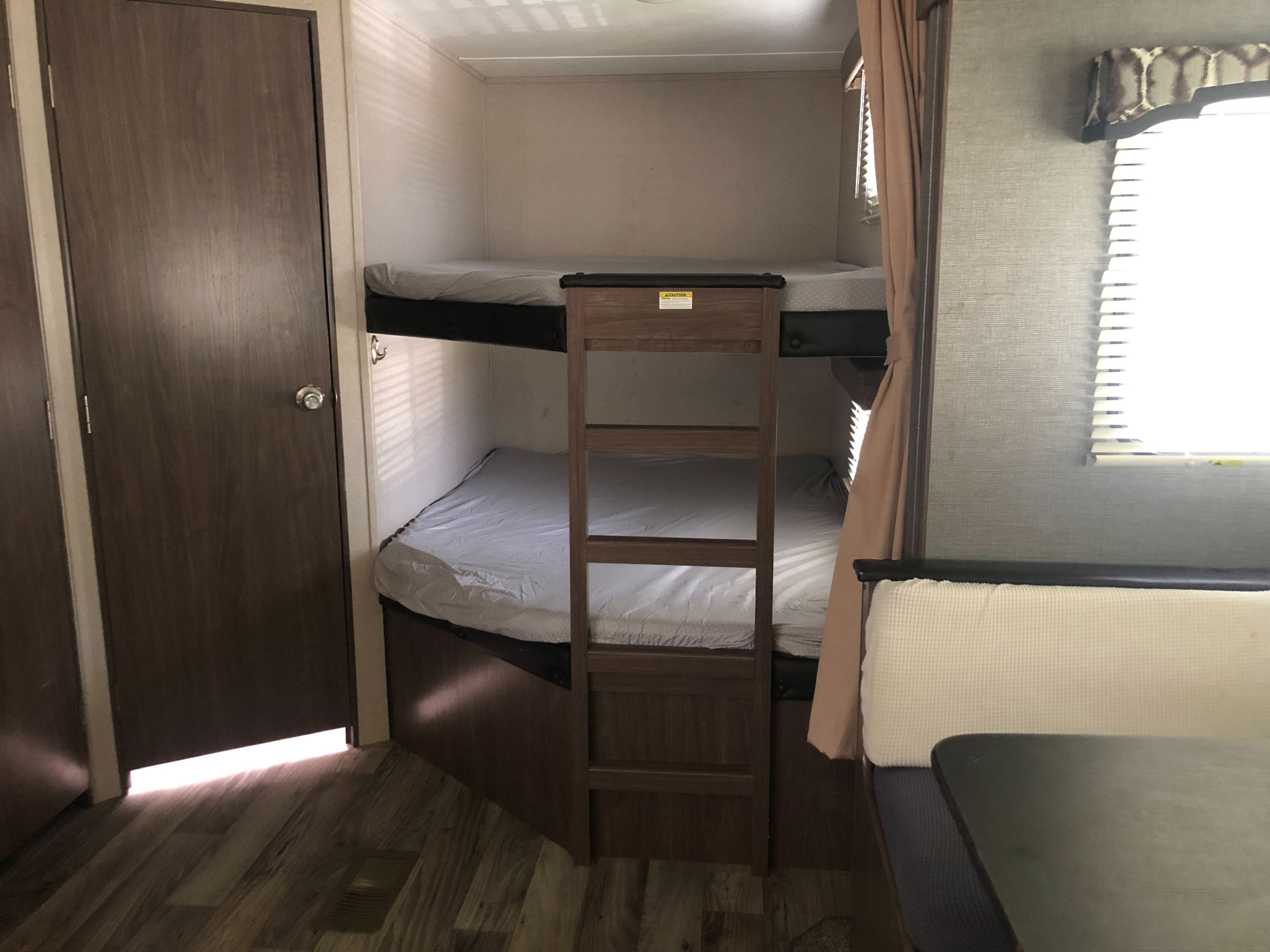 RV rental interior: bunk beds with ladder, door, window, and a dinette for comfy family travel.. Keystone RV Hideout 2019