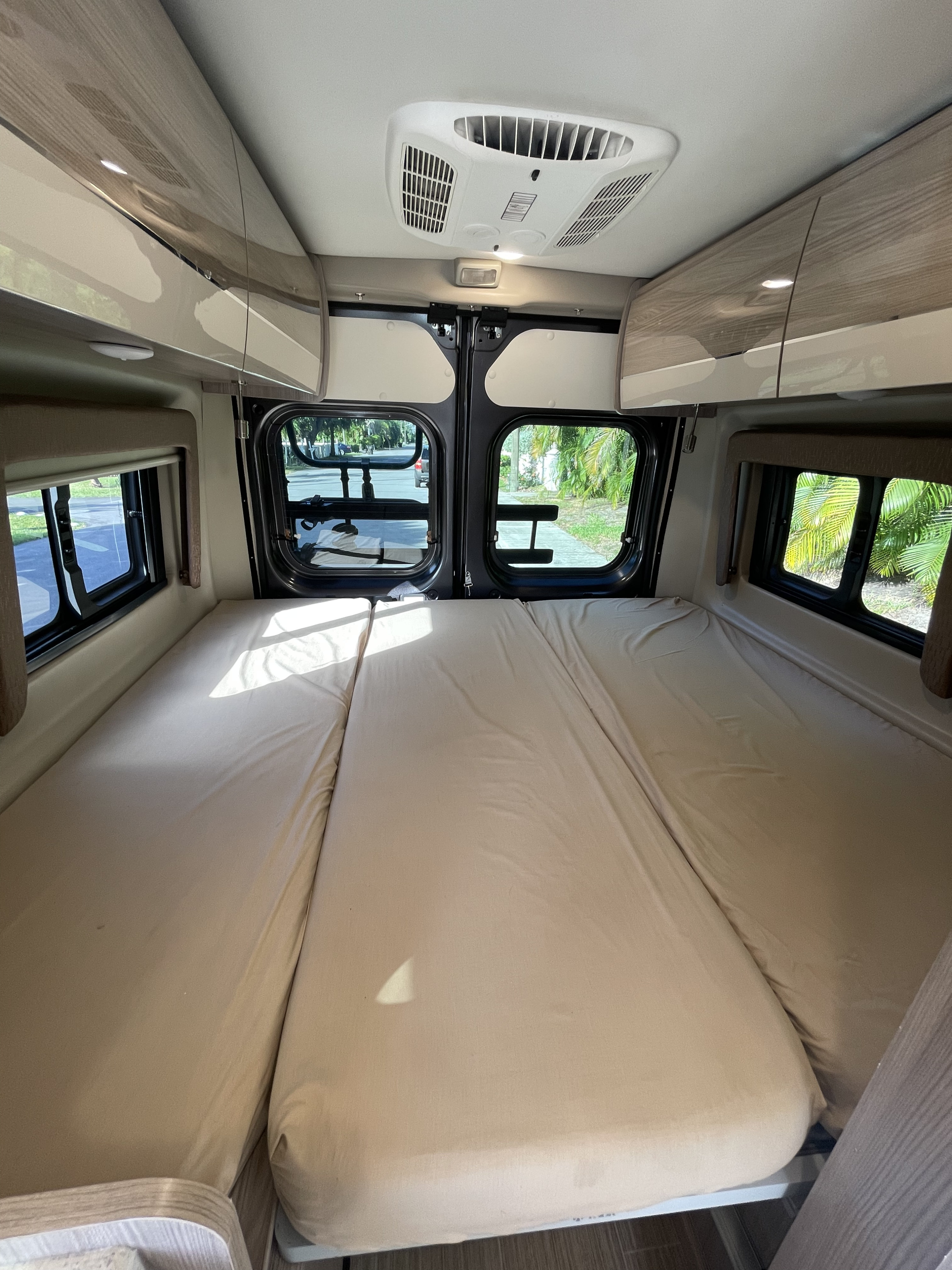 Spacious RV rental interior with comfortable bed setup. Features overhead storage, AC, and large windows for a cozy camper experience.. Thor Sequence 2022
