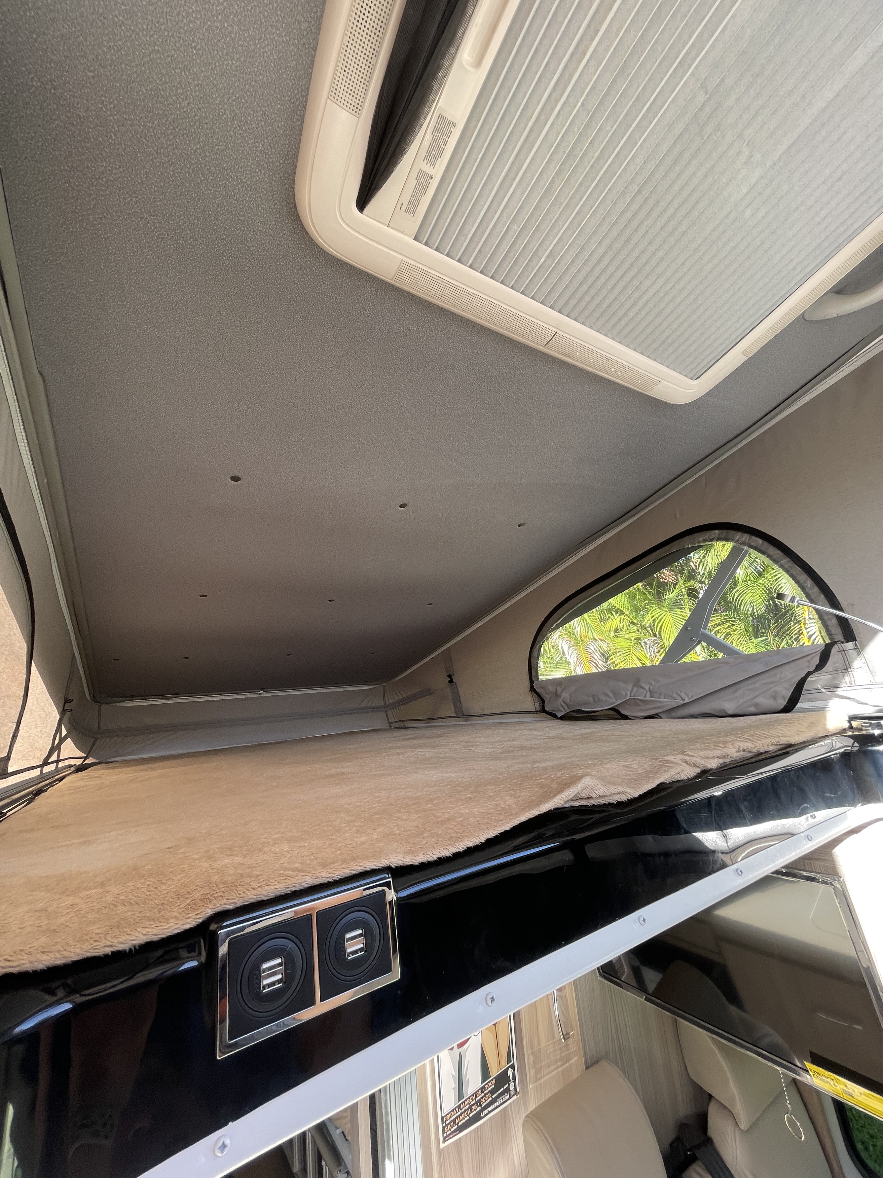 Inside an RV rental: a cozy pop-top sleeping area with soft bedding, skylight, and convenient USB charging ports.. Thor Sequence 2022