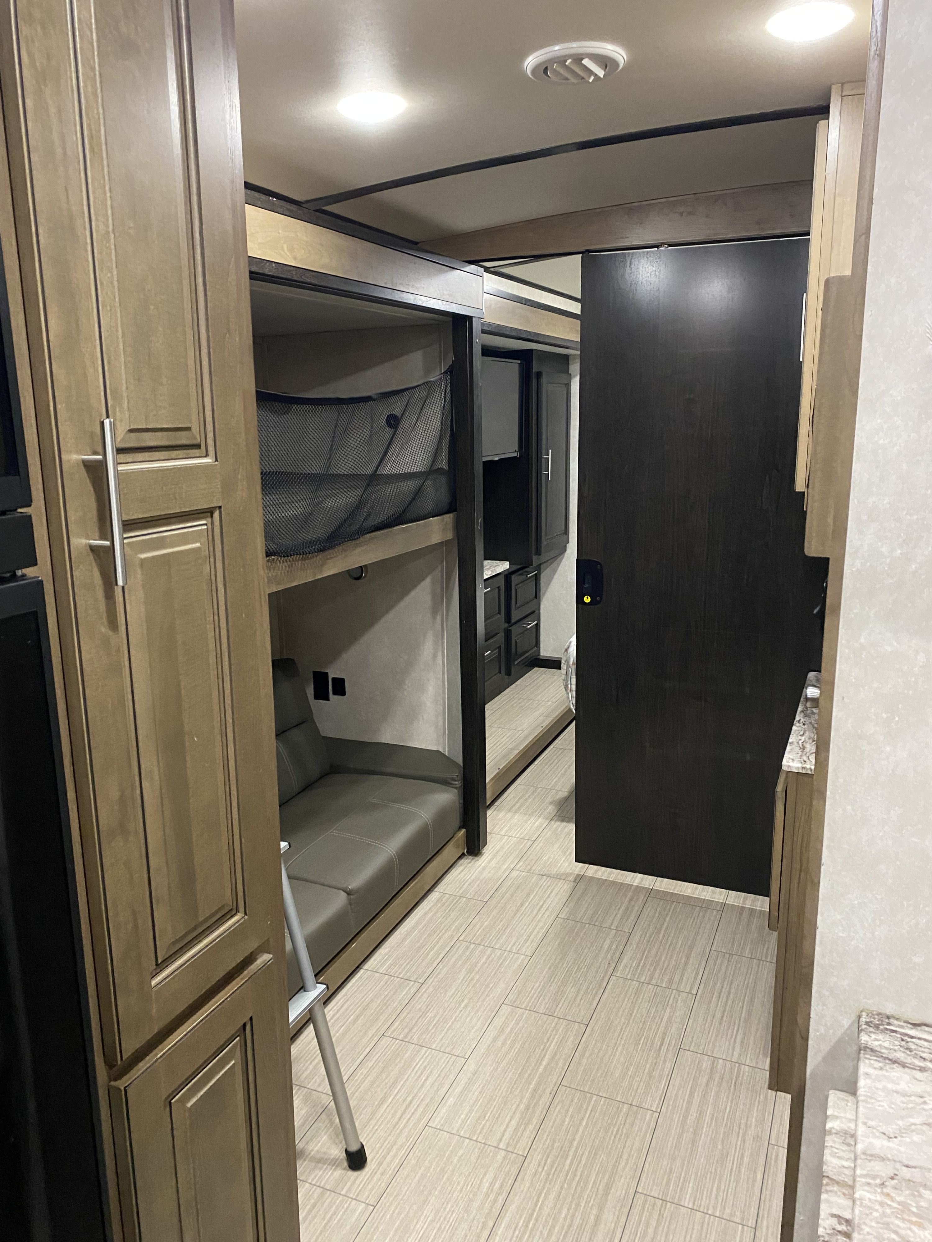 This modern RV rental interior features a bunkhouse with cozy seating below a bunk bed, cabinetry, and a tiled hallway.. FR3 FR3 Motorhome 2021