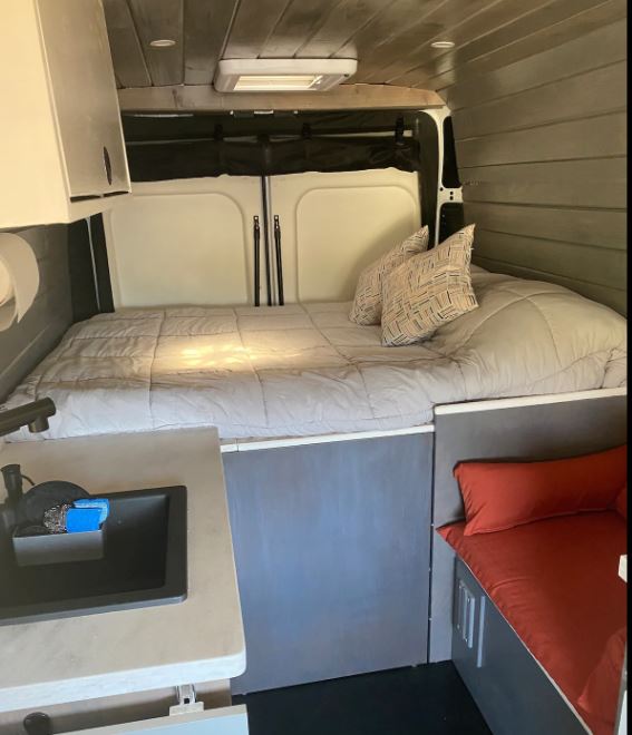Cozy RV rental camper van interior featuring a bed, small kitchen sink, and seating area.. Other Other 2021