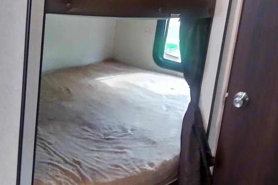 A simple RV rental sleeping nook with a mattress, window, and a dark curtain for privacy.. Jayco Jay Flight 2019