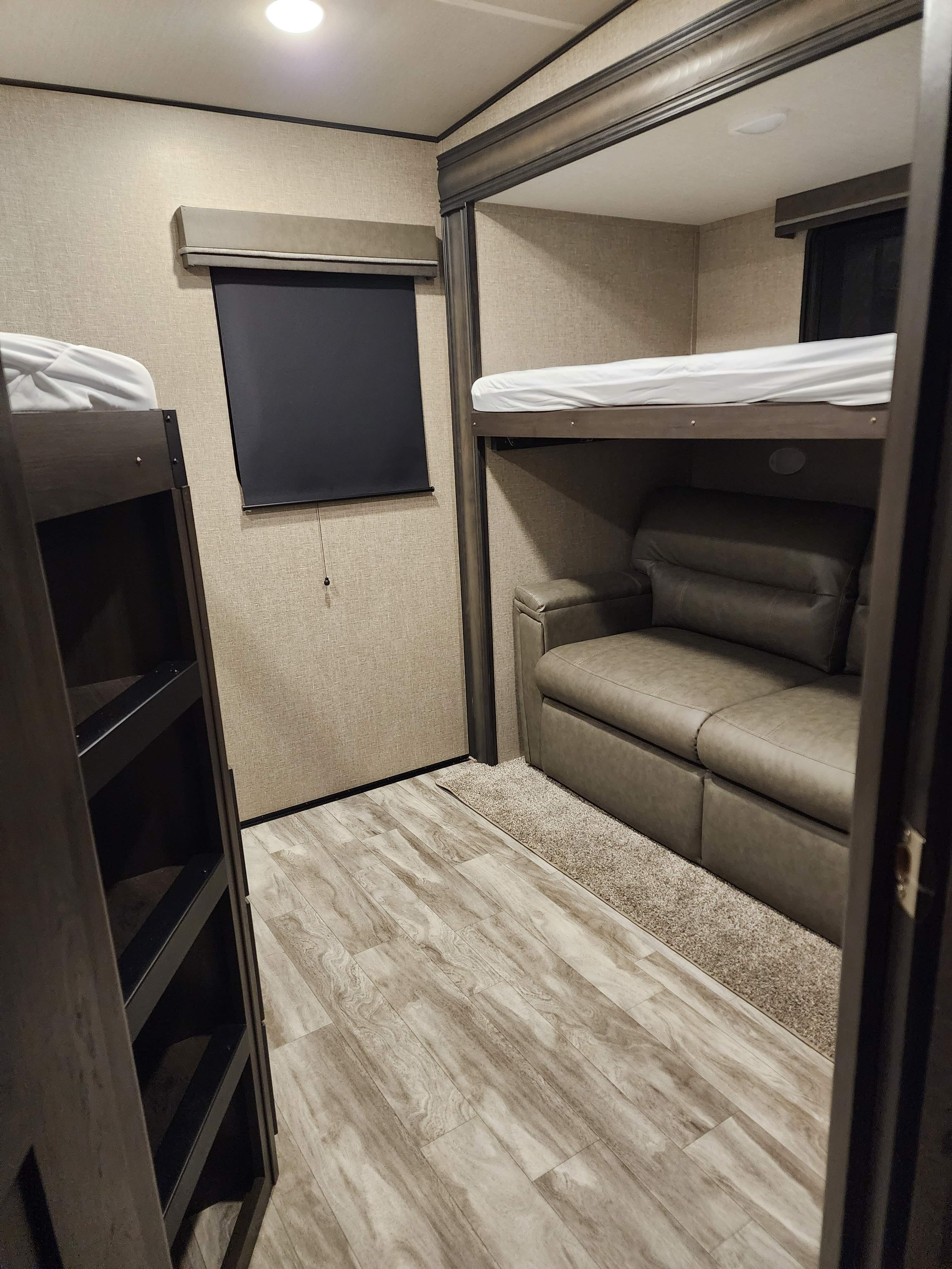 Spacious RV rental interior with bunk beds, a sofa, and wood-look flooring, offering comfortable living space.. Grand Design Reflection 2022