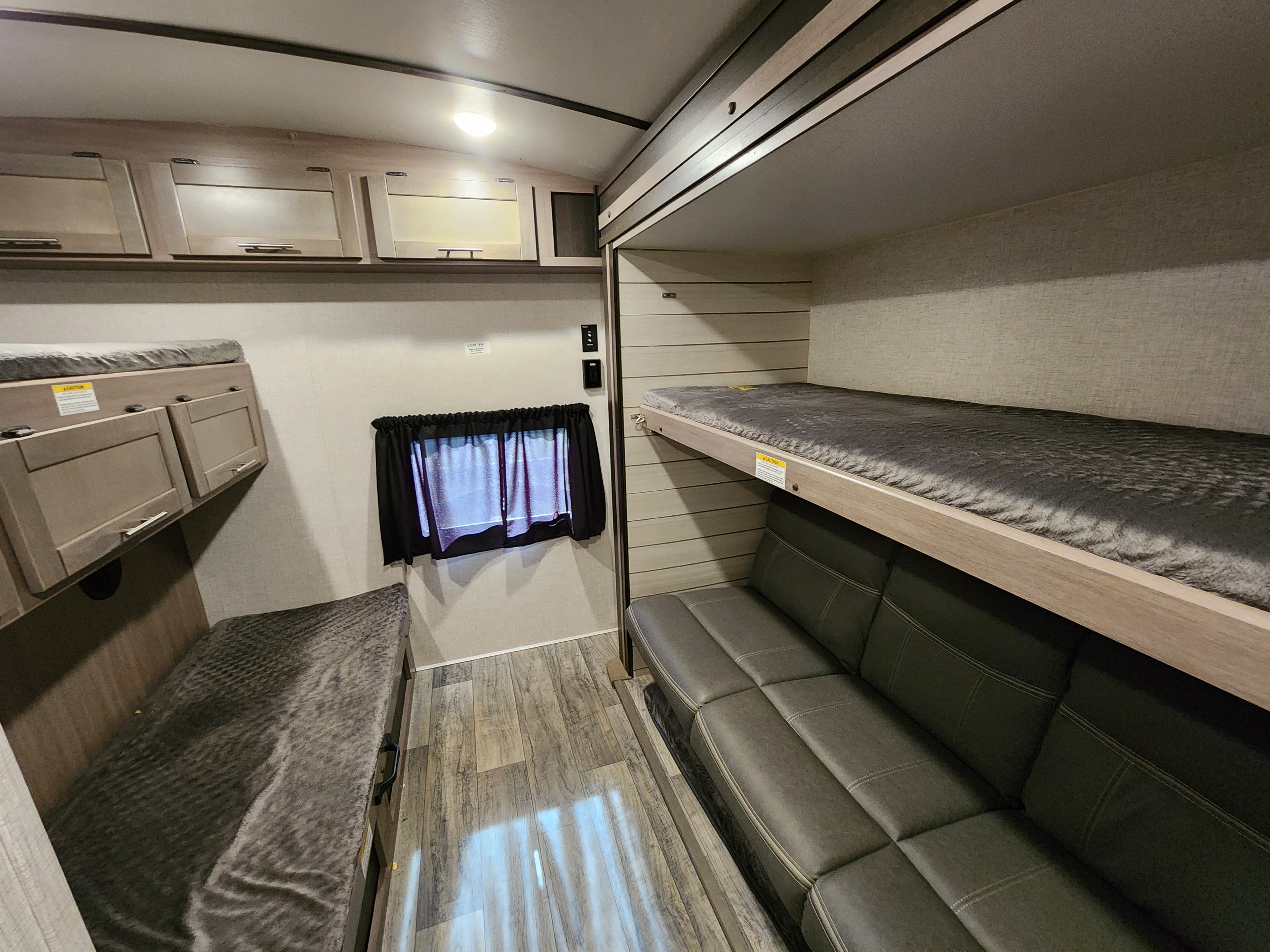 An RV rental's inviting bunk bed area with a comfortable sofa and overhead cabinets, perfect for travel.. Crossroads Sunset Trail 2021