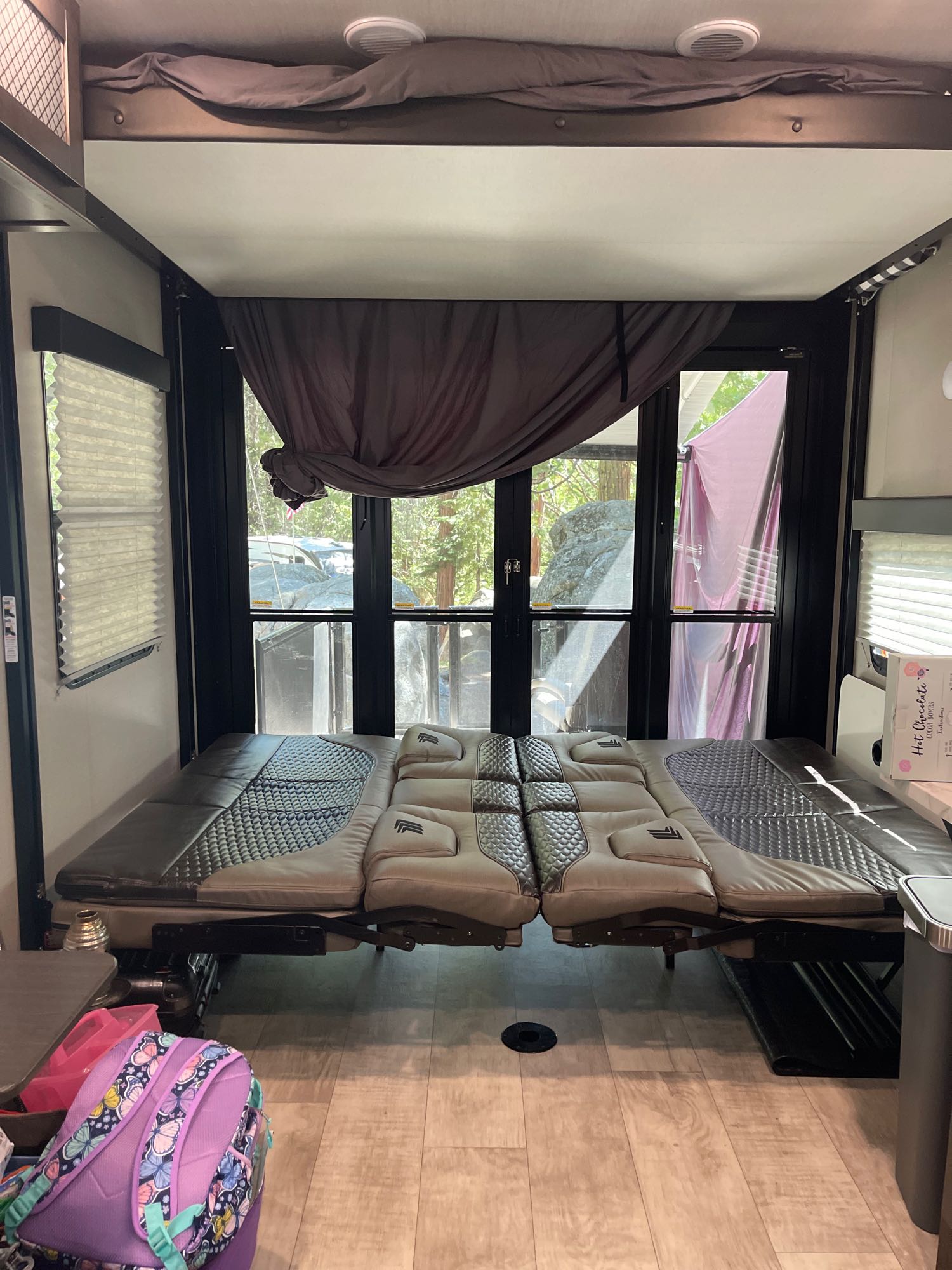 Inside an RV rental: a flexible bed/couch setup fills the rear, with a large window revealing a rocky, wooded outdoor scene.. Grand Design Momentum 2022