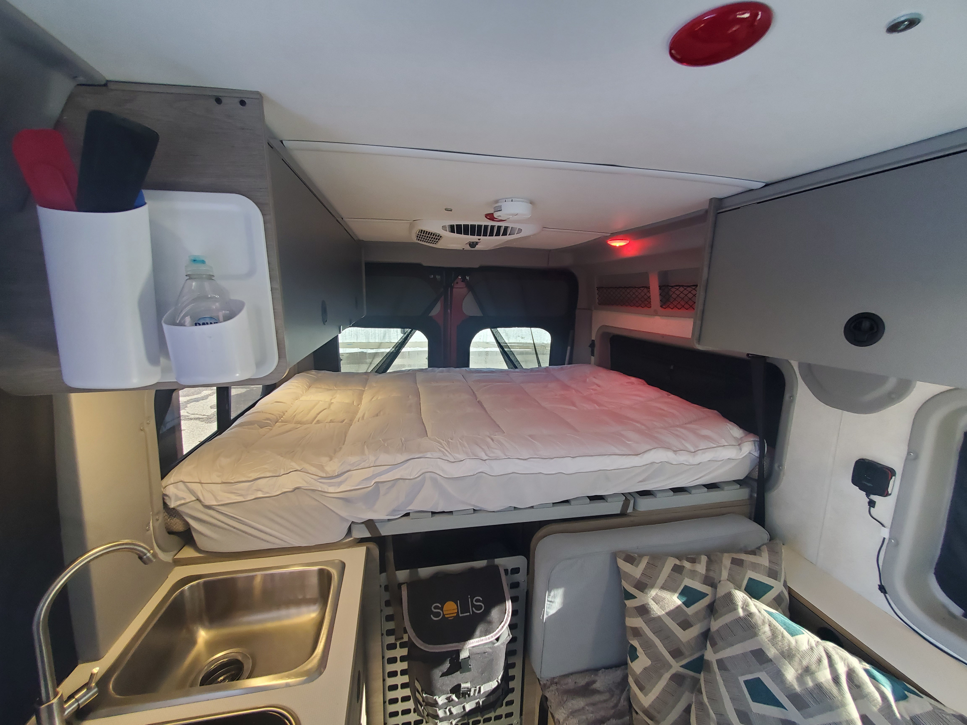 Inside an RV rental featuring a comfy bed, kitchen sink, overhead storage, and geometric pillows.. Winnebago Solis Pocket 2022