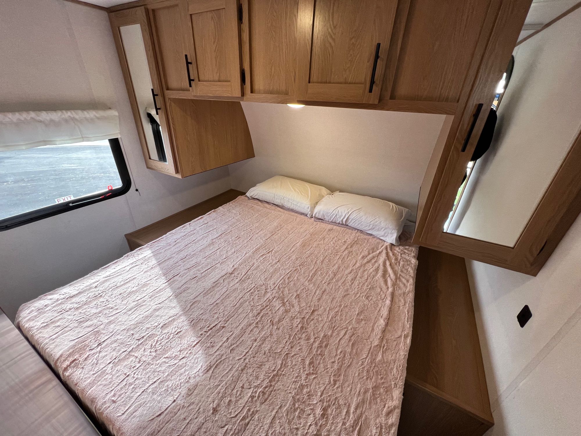 Cozy RV rental bedroom with bed, wooden cabinets, and window with an EXIT sign. Perfect for road trips.. Prime Time Avenger 2022