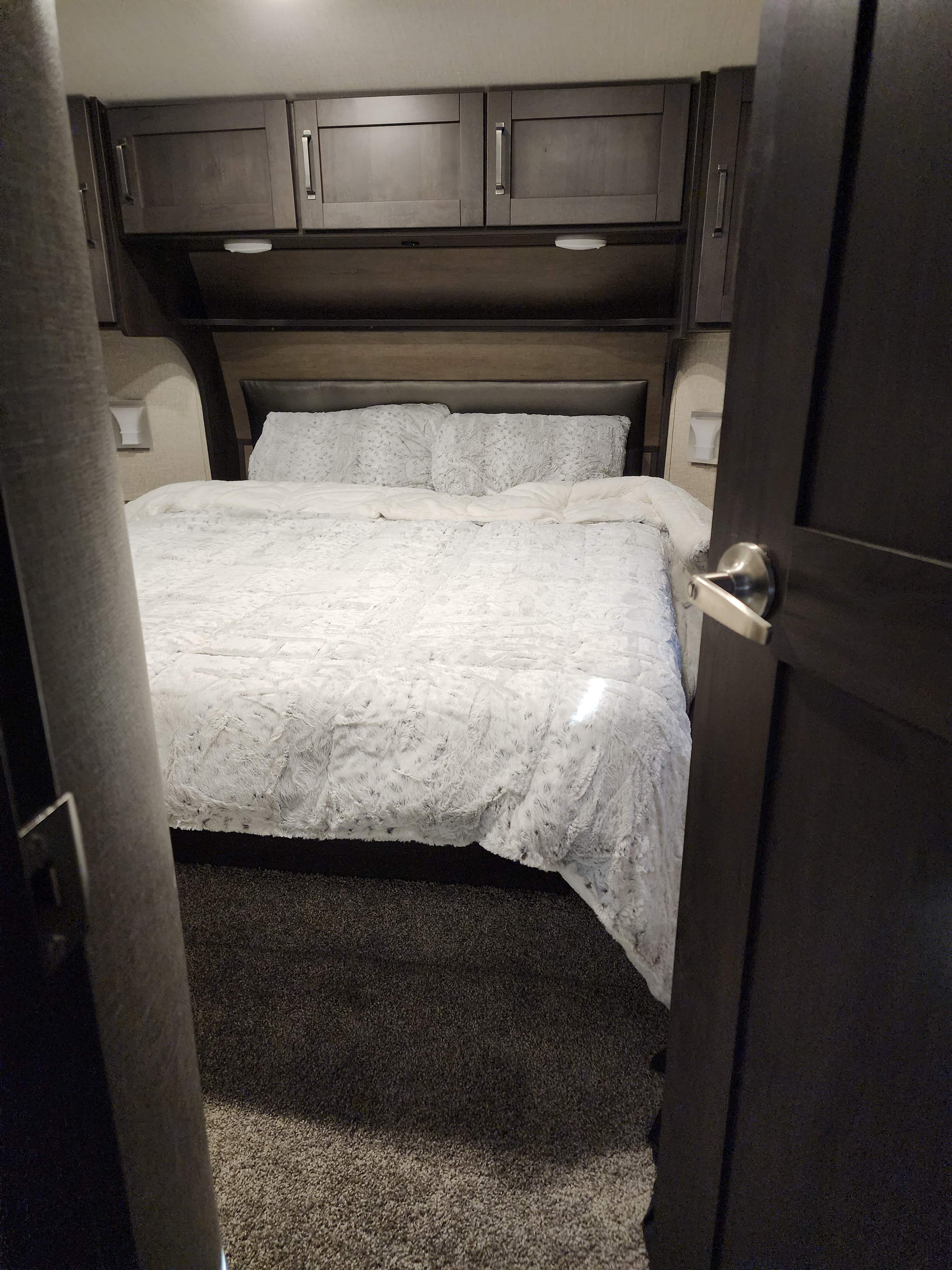 Inside an RV rental: a compact bedroom with an inviting bed, matching pillows, and functional overhead storage cabinets.. Grand Design Reflection 2022