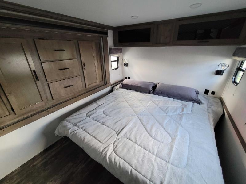 Experience comfort in this RV rental's bedroom, featuring a spacious bed, overhead cabinets, and built-in drawers.. Forest River Saber 2022