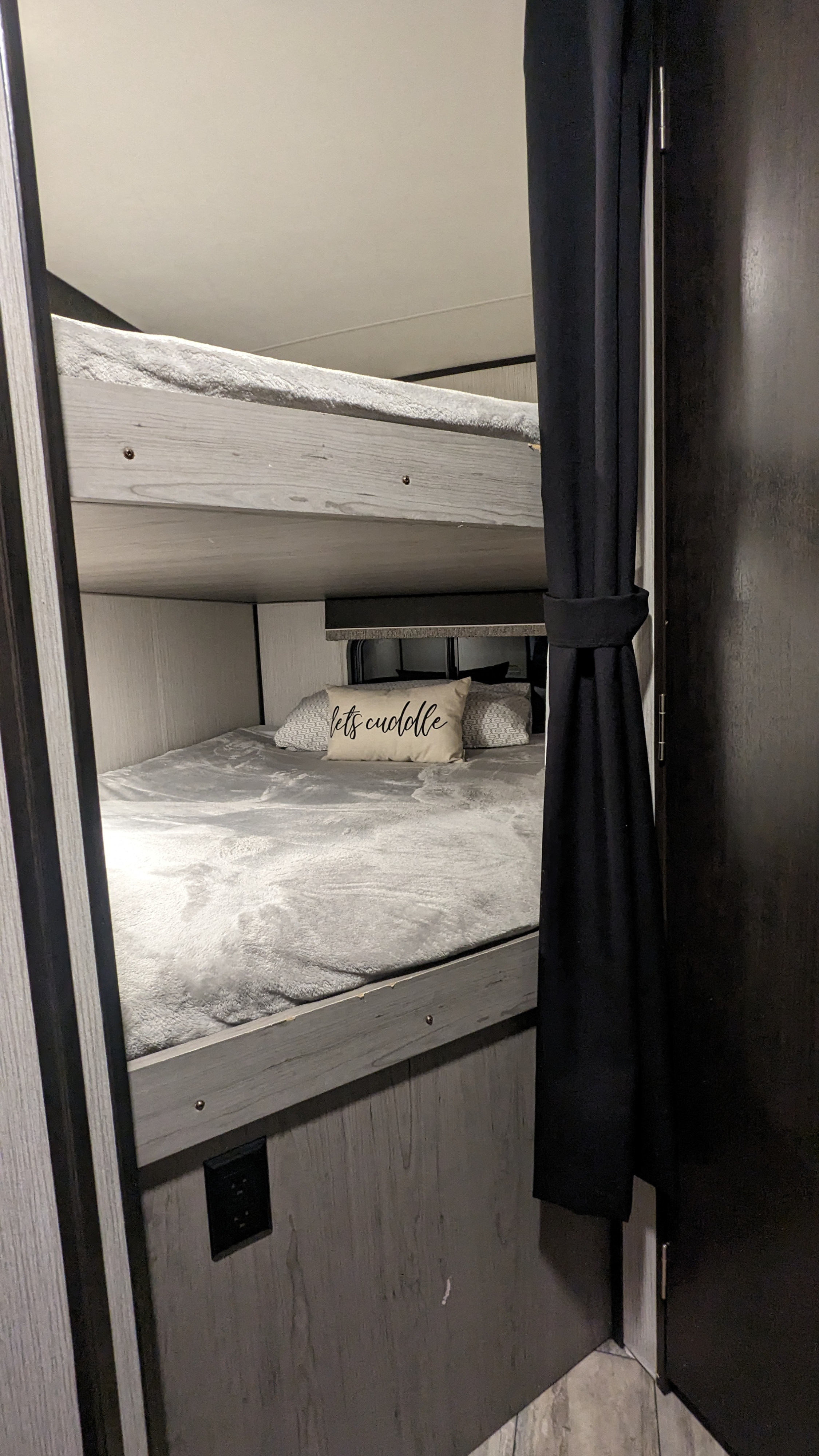 Inside an RV rental, two cozy bunk beds with soft grey bedding and a "lets cuddle" pillow await, offering comfortable sleeping.. Heartland RVs North Trail 2021