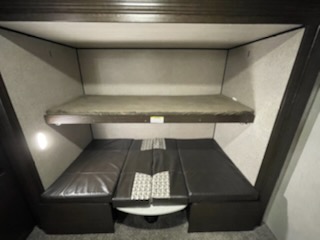 Inside an RV rental, this bunk bed area features a top bunk over a lower convertible dinette/bed with black cushions.. prowler 33PBHS 2019