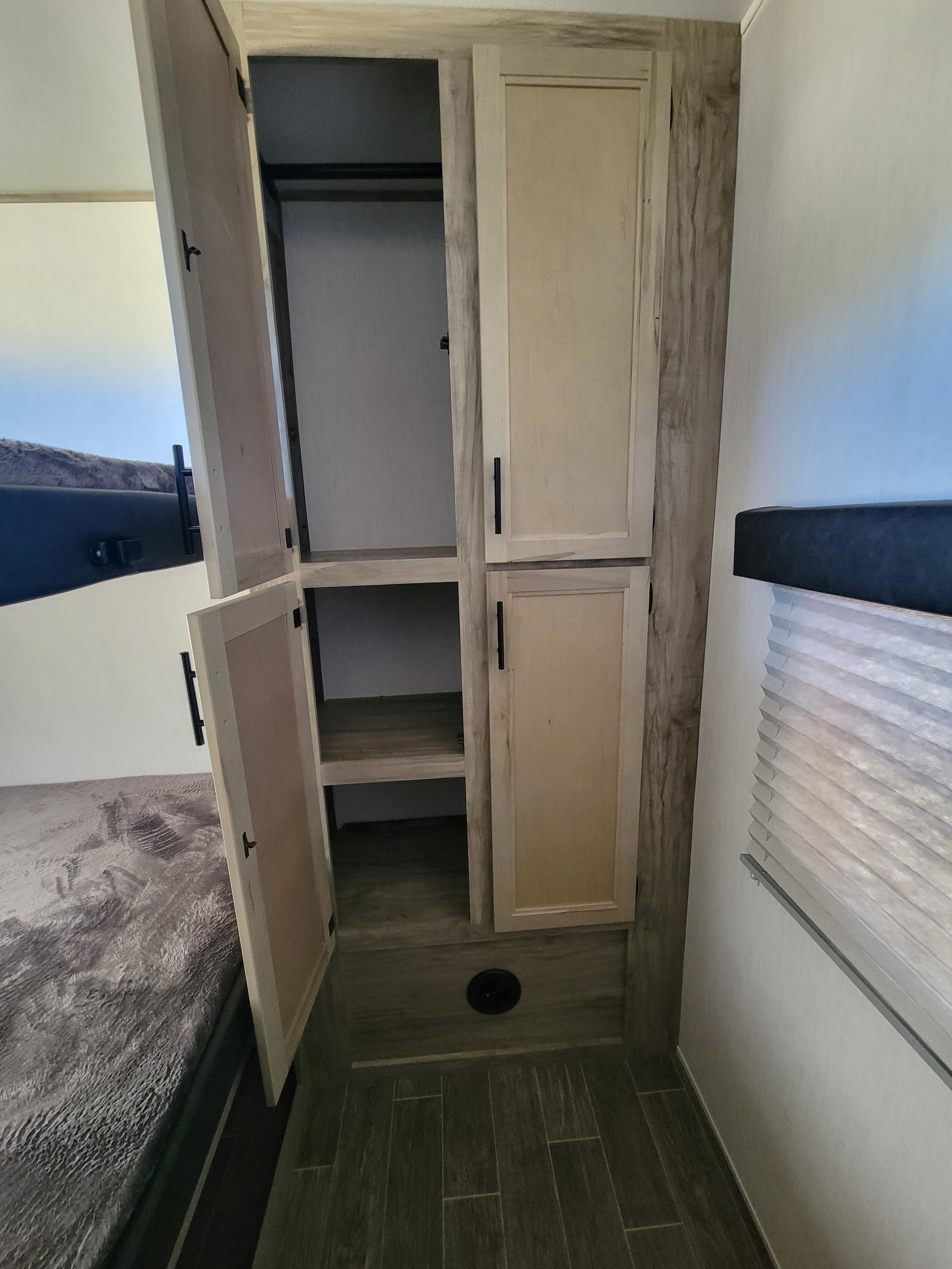 RV rental bedroom storage: Open wardrobe with shelves, hanging bar, and floor space, useful for travel organization.. Forest River Cherokee Arctic Wolf 2022