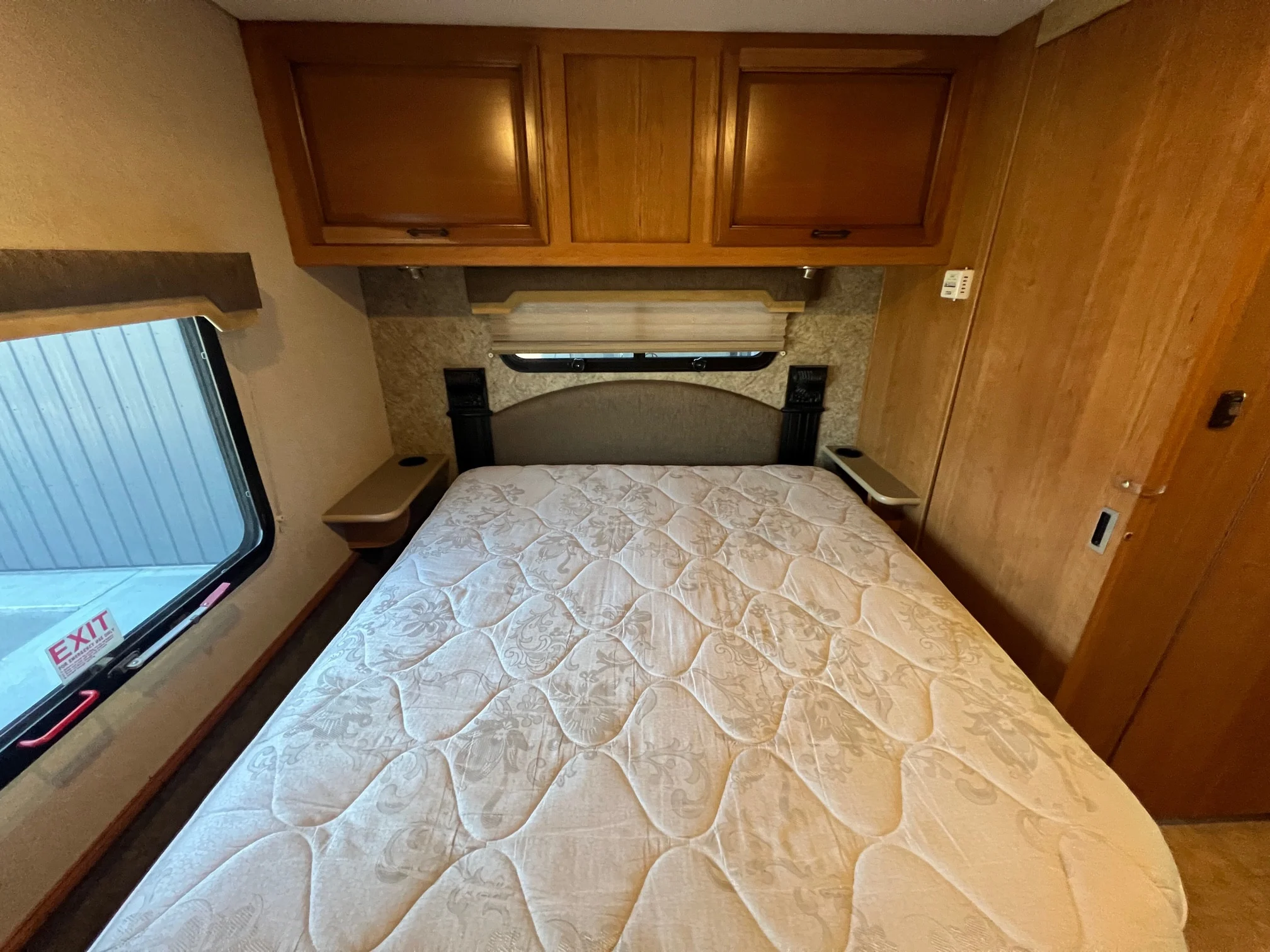 Cozy RV rental bedroom interior features a comfortable bed, overhead cabinets, and an emergency exit window.. Fleetwood Storm 2016