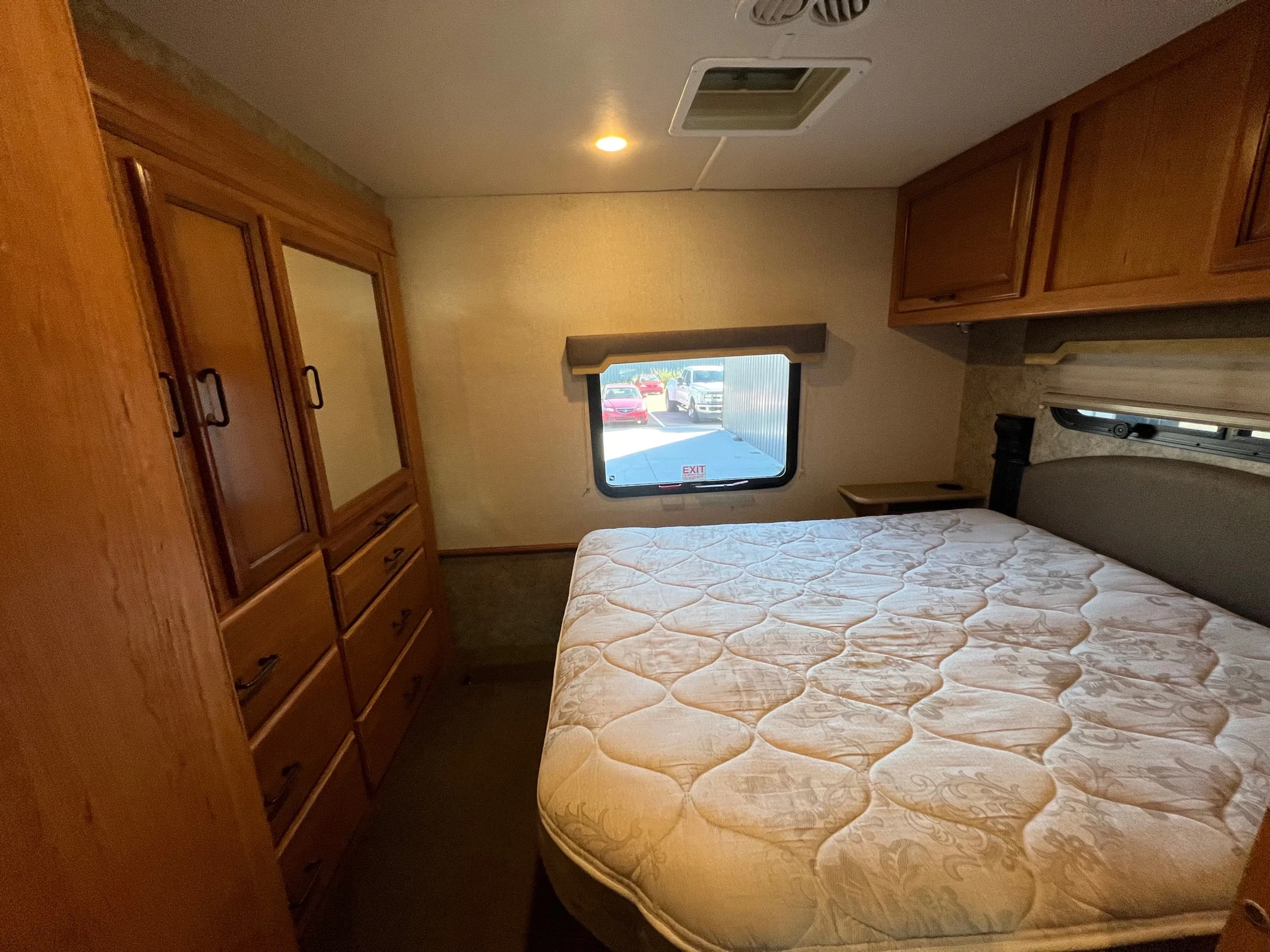 RV rental bedroom: patterned mattress, wood wardrobe, overhead cabinets, and window. A compact, cozy space.. Fleetwood Storm 2016