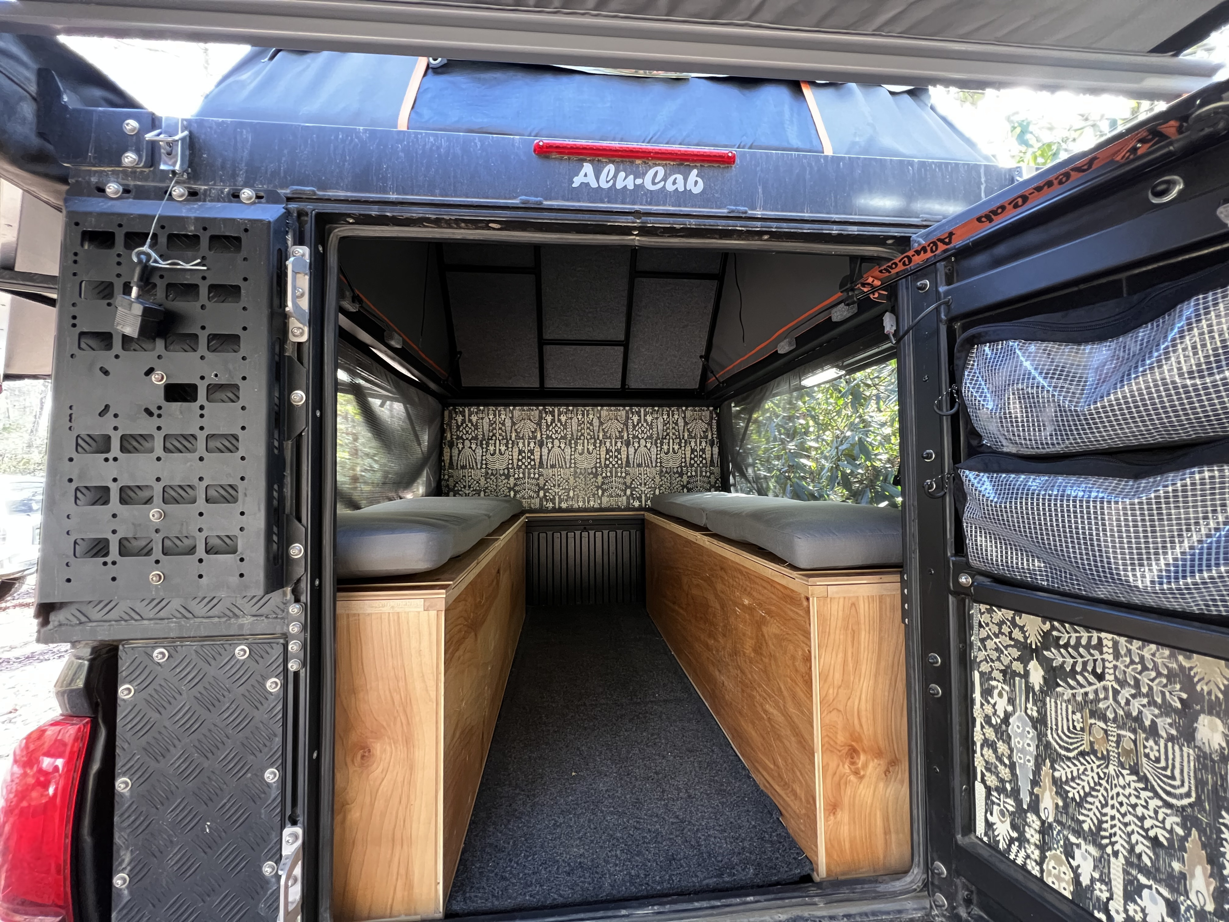 Step inside this Alu-Cab RV rental, featuring a cozy truck camper interior with custom wood storage, beds, and patterned walls.. Toyota Tacoma 2020