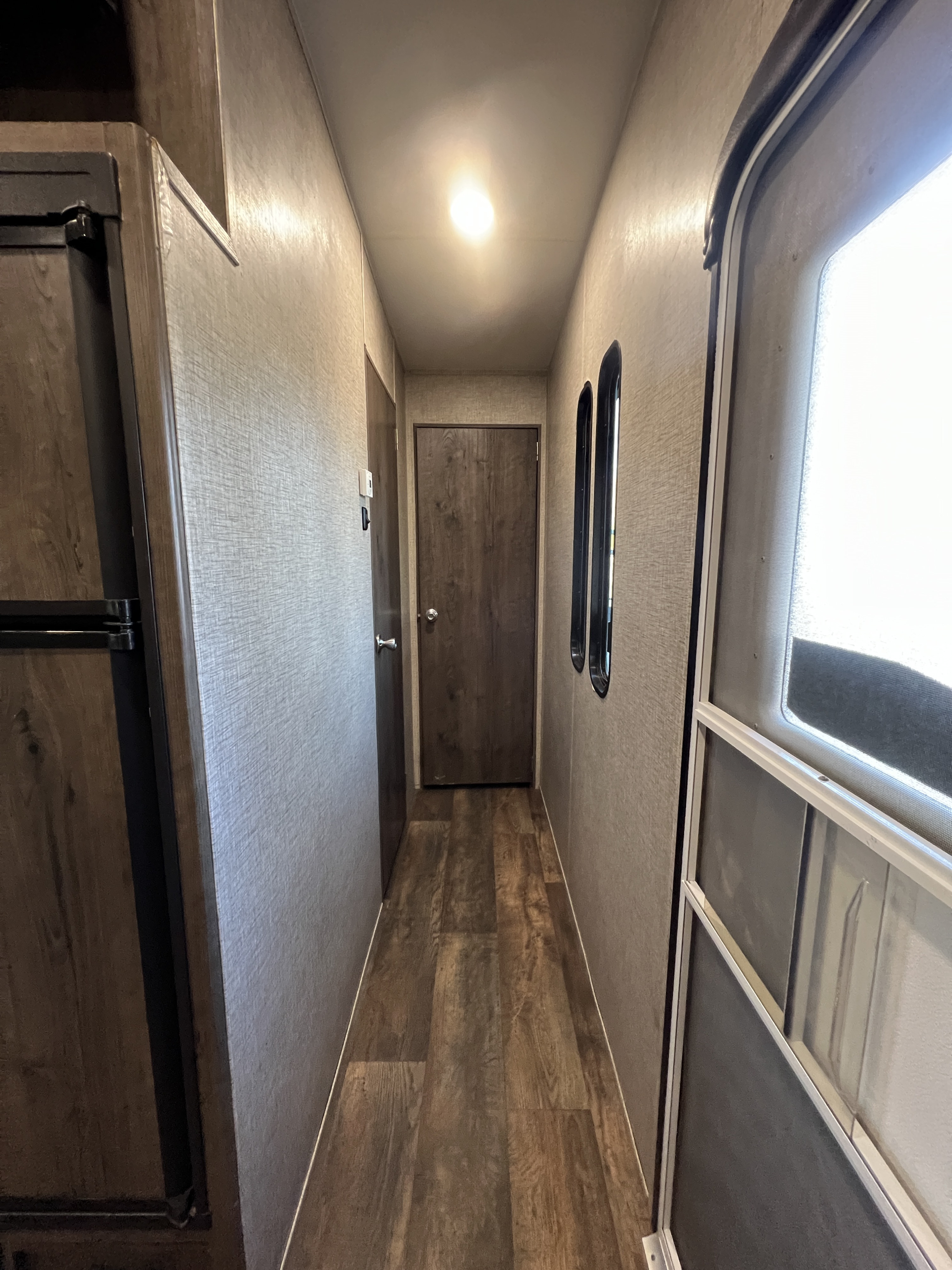 RV rental interior: A bright, narrow hallway with wood floors, a refrigerator, doors, and oval windows leading outside.. Eclipse Recreational Vehicles Stellar 2016