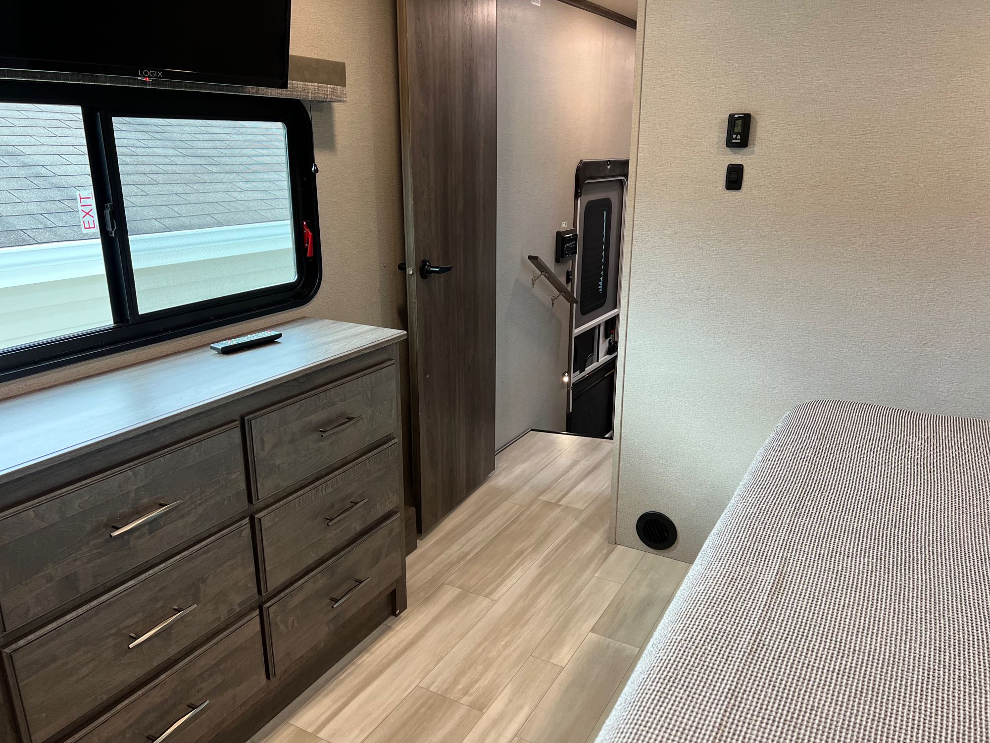Step inside this RV rental: bedroom area with a dresser, TV, and emergency exit window, leading to stairs.. Grand Design Solitude S-Class 2022