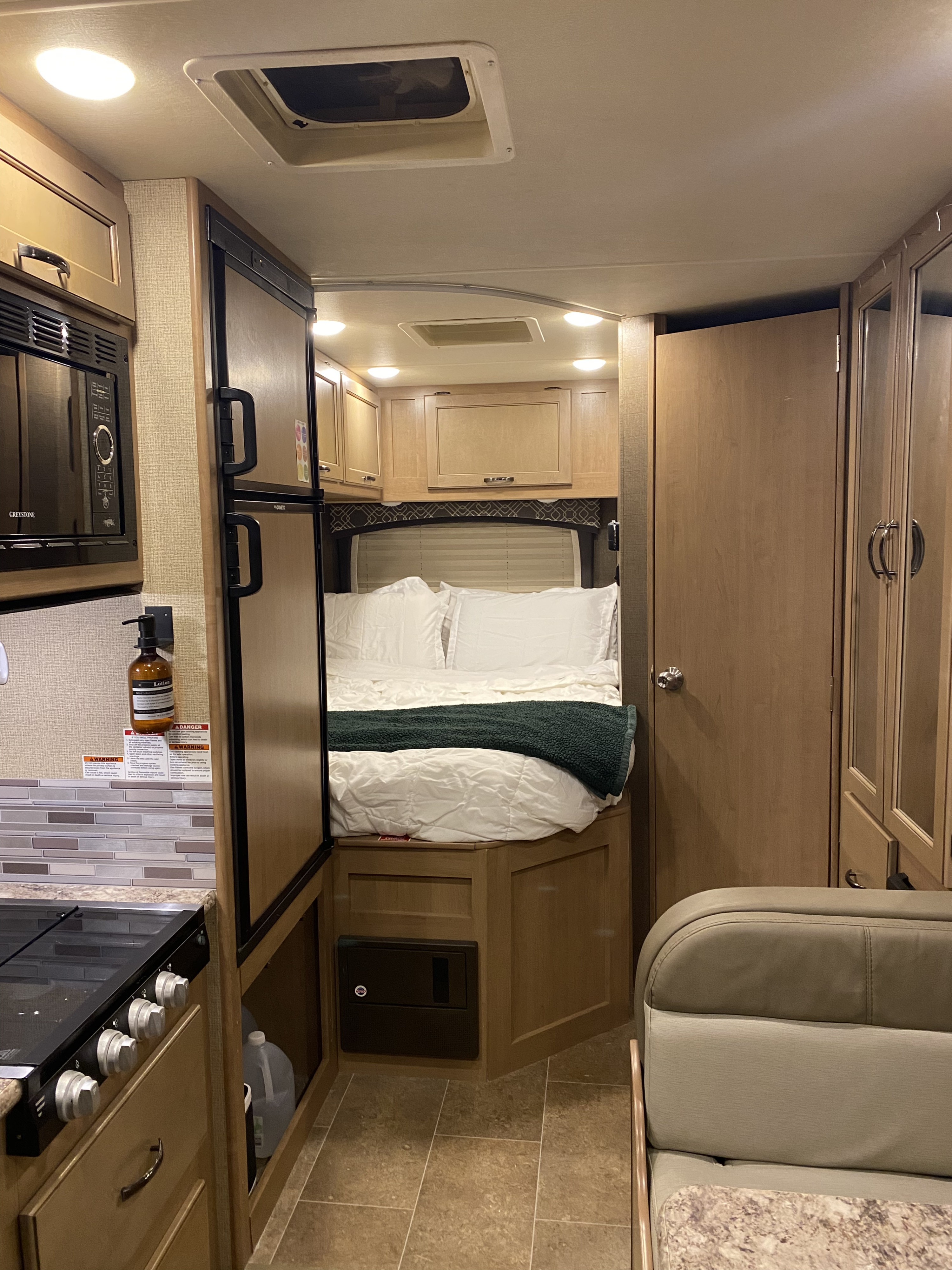 Cozy RV rental interior showing a compact kitchen with stove & microwave, a comfortable bedroom, and dinette seating.. Thor Chateau 2019