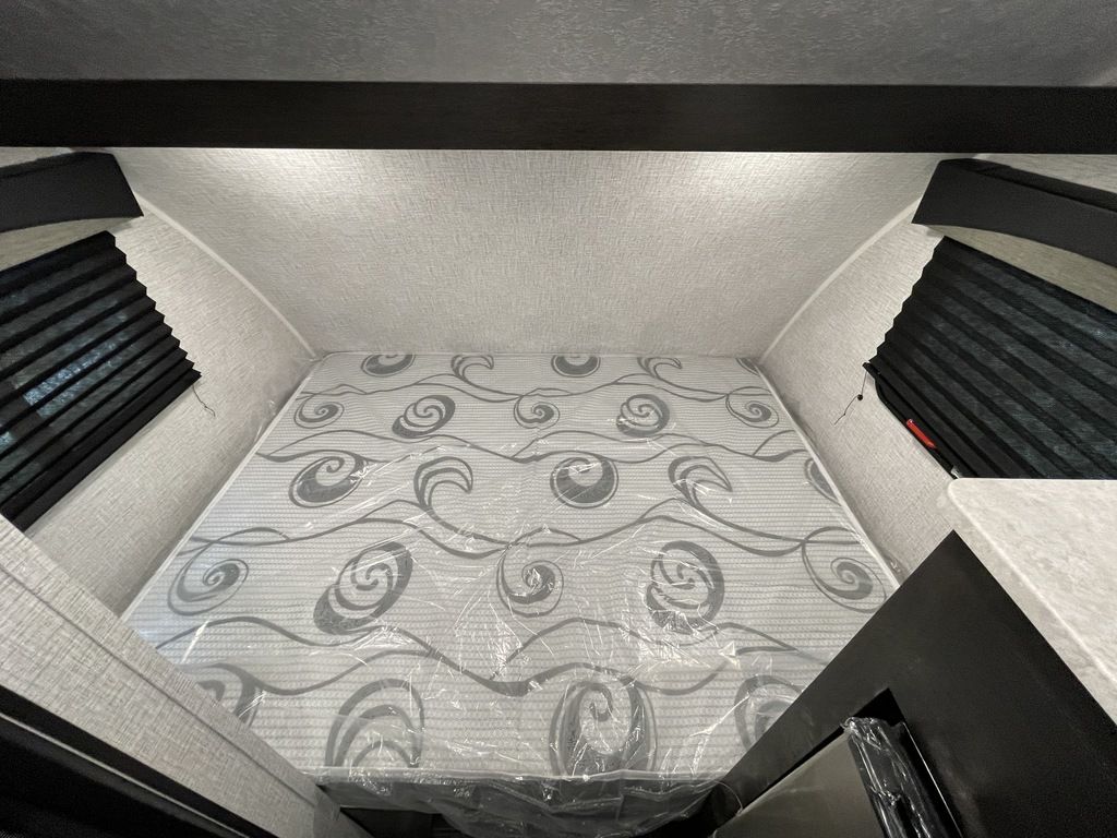 Inside an RV rental: a clean, new mattress in its plastic wrap in a cozy sleeping alcove with side windows.. Braxton Creek BUSHWHACKER PLUS 17FD 2022