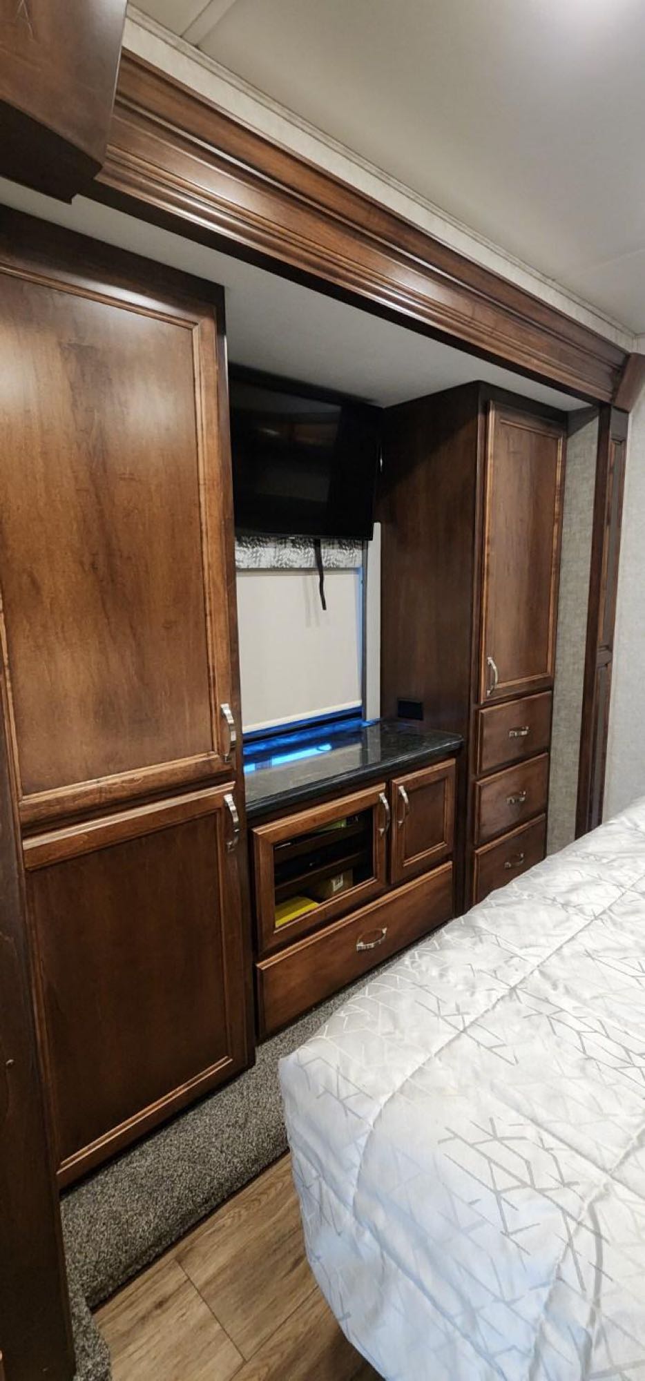 Experience comfort in this RV rental bedroom: dark wood cabinetry, built-in TV, cozy bed, and ample storage.. Renegade Custom Coaches Verona 2022