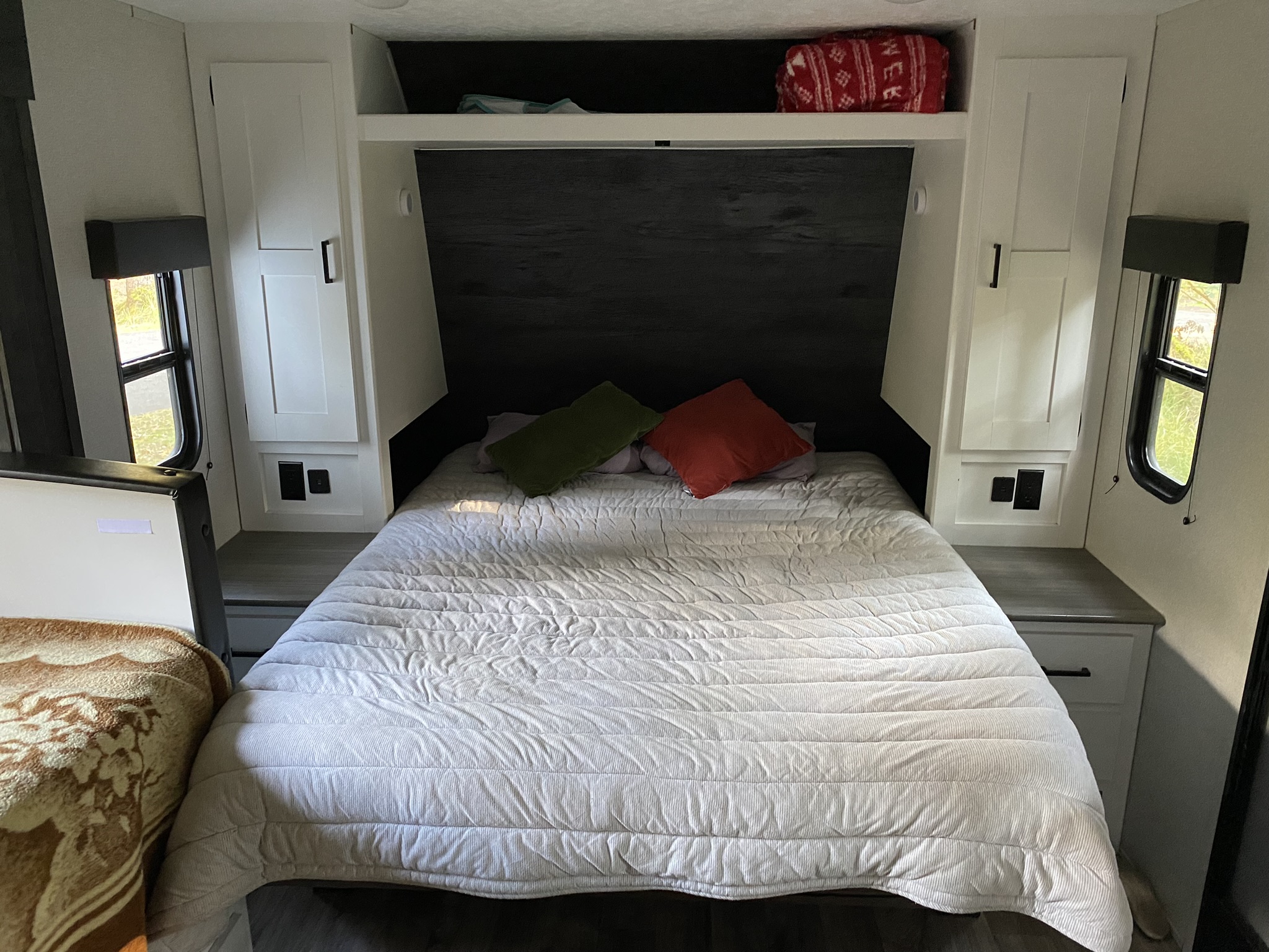 Cozy RV rental bedroom with a comfortable bed, dark headboard, overhead storage, and side cabinets.. Keystone RV Hideout 2021