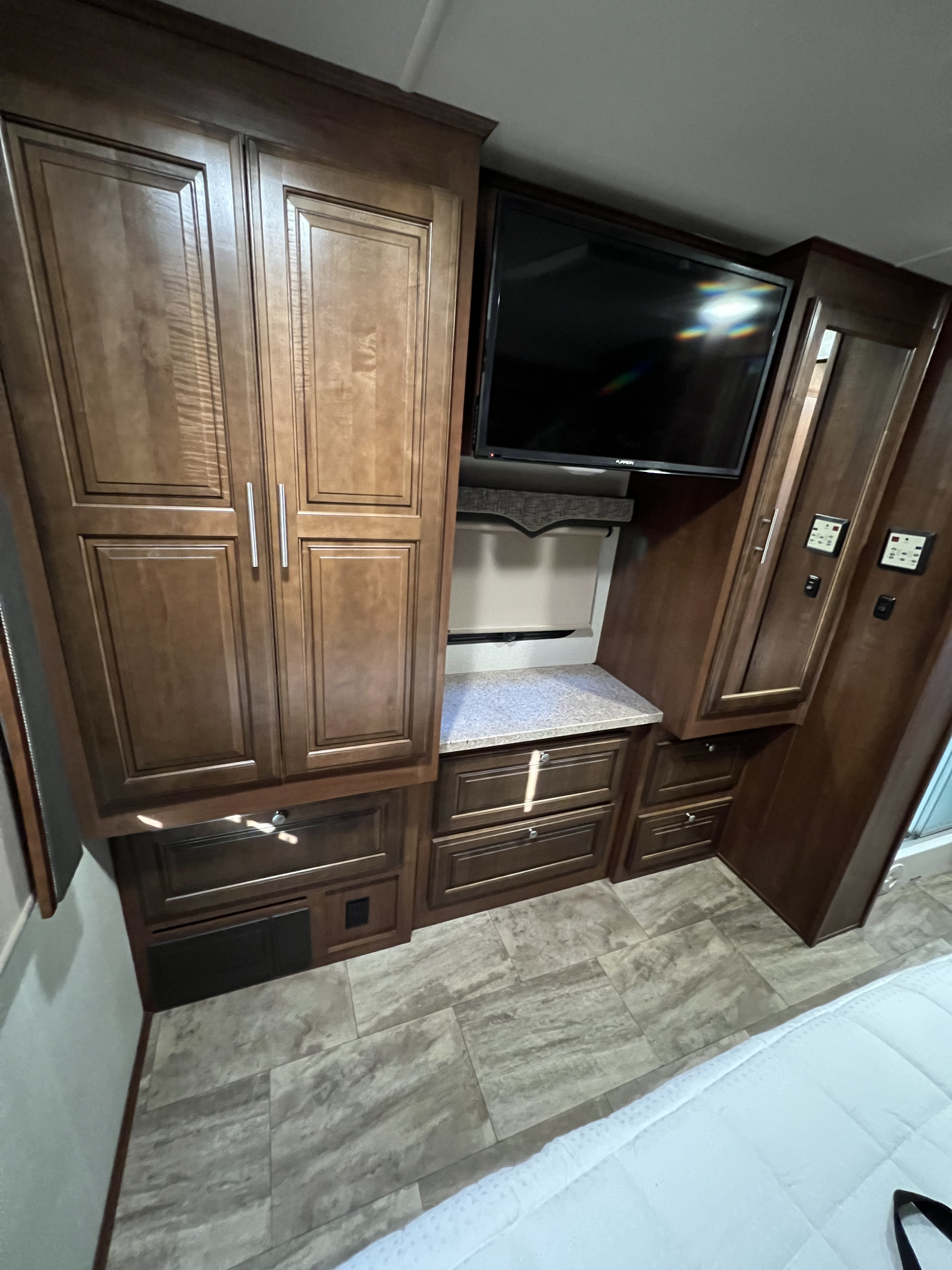This RV rental features a cozy bedroom with dark wood cabinetry, a mounted TV, ample storage, and a light-colored countertop.. Georgetown GT5 2018