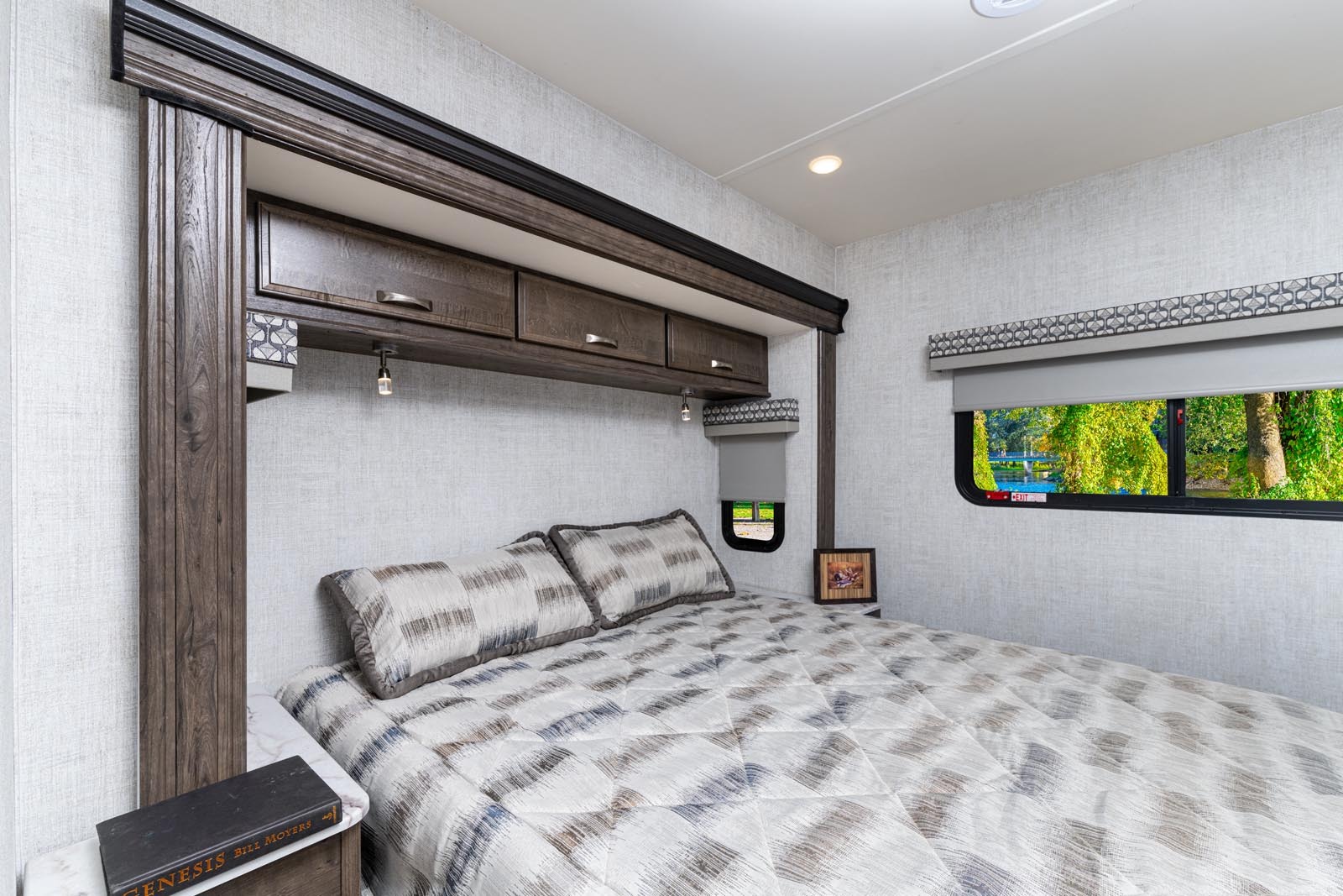Cozy RV rental bedroom interior features overhead cabinets, a comfortable bed, and a window with a scenic nature view.. Gulf Stream Conquest 6320D 2023