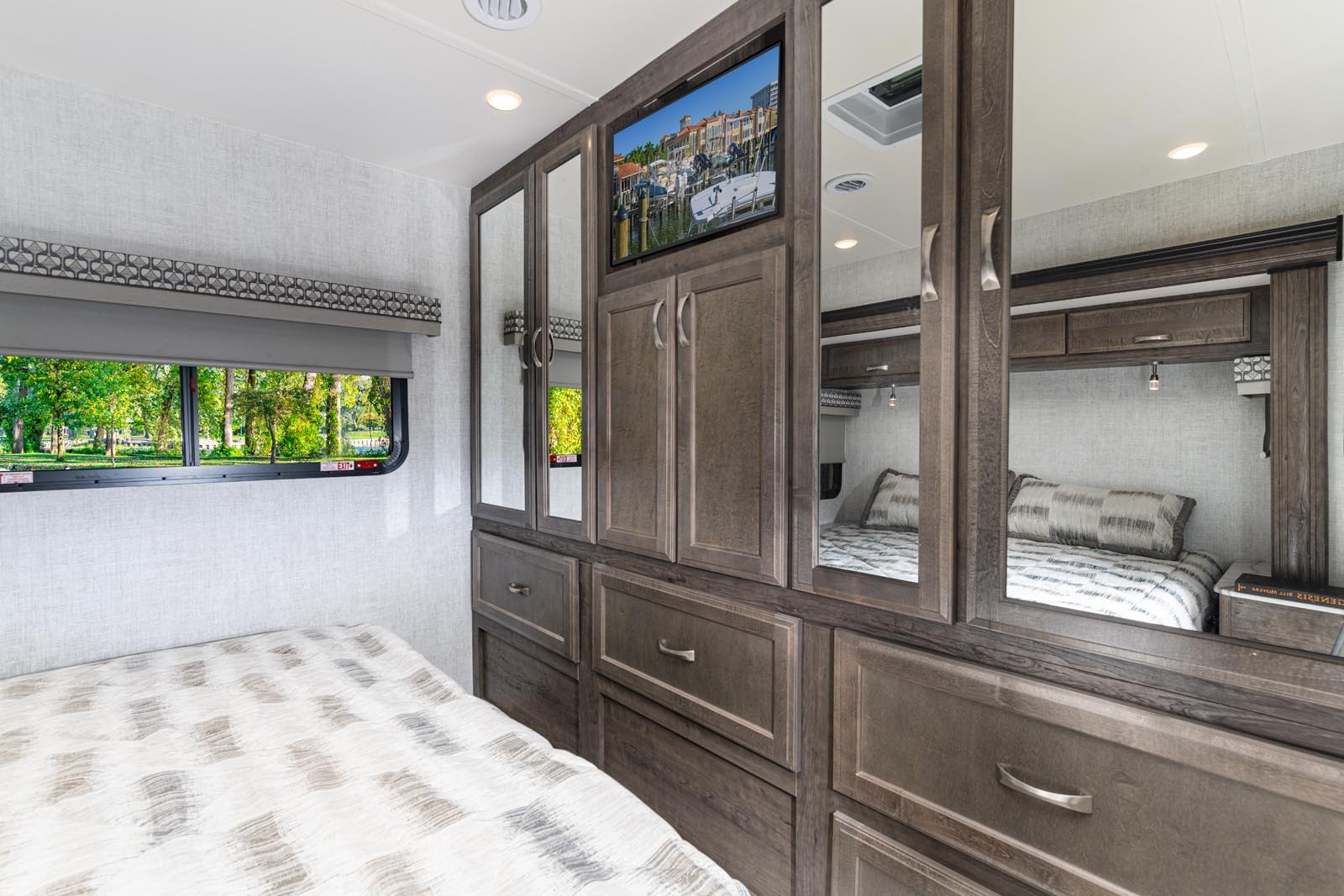 Spacious RV rental bedroom featuring a bed, ample wood cabinetry, mirrors, and a wall-mounted TV for comfortable travel.. Gulf Stream Conquest 6320D 2023