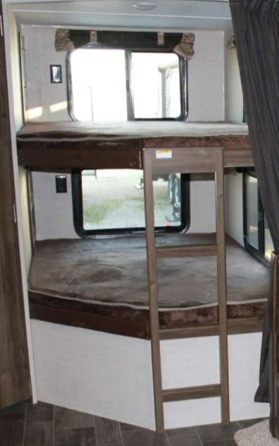 Inside an RV rental, comfortable bunk beds are shown with windows and a ladder, ready for family adventures.. Keystone RV Bullet Ultra Lite 2016