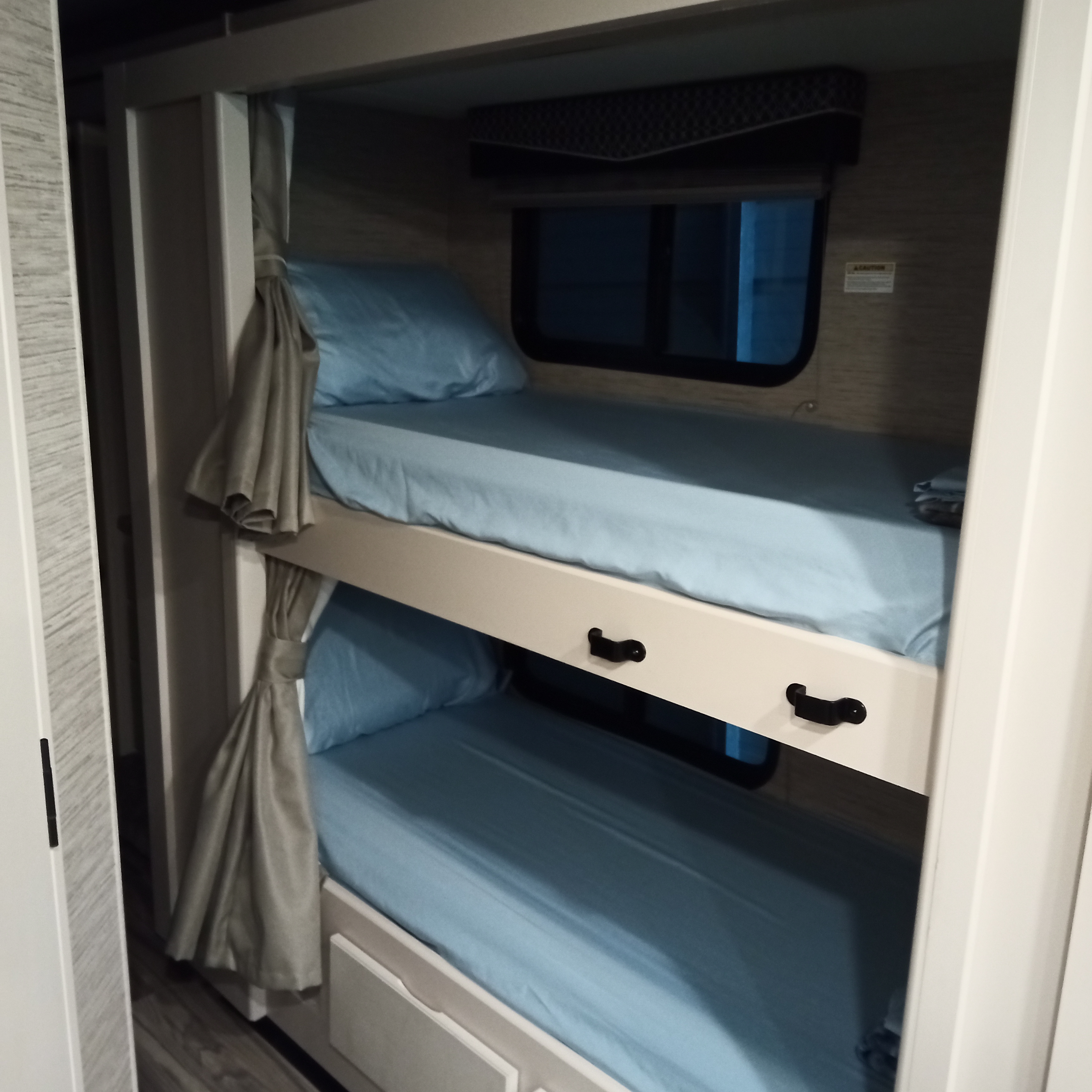 Inside an RV rental: cozy bunk beds with light blue sheets, windows, and curtains for comfortable sleeping.. Thor Four Winds 2022