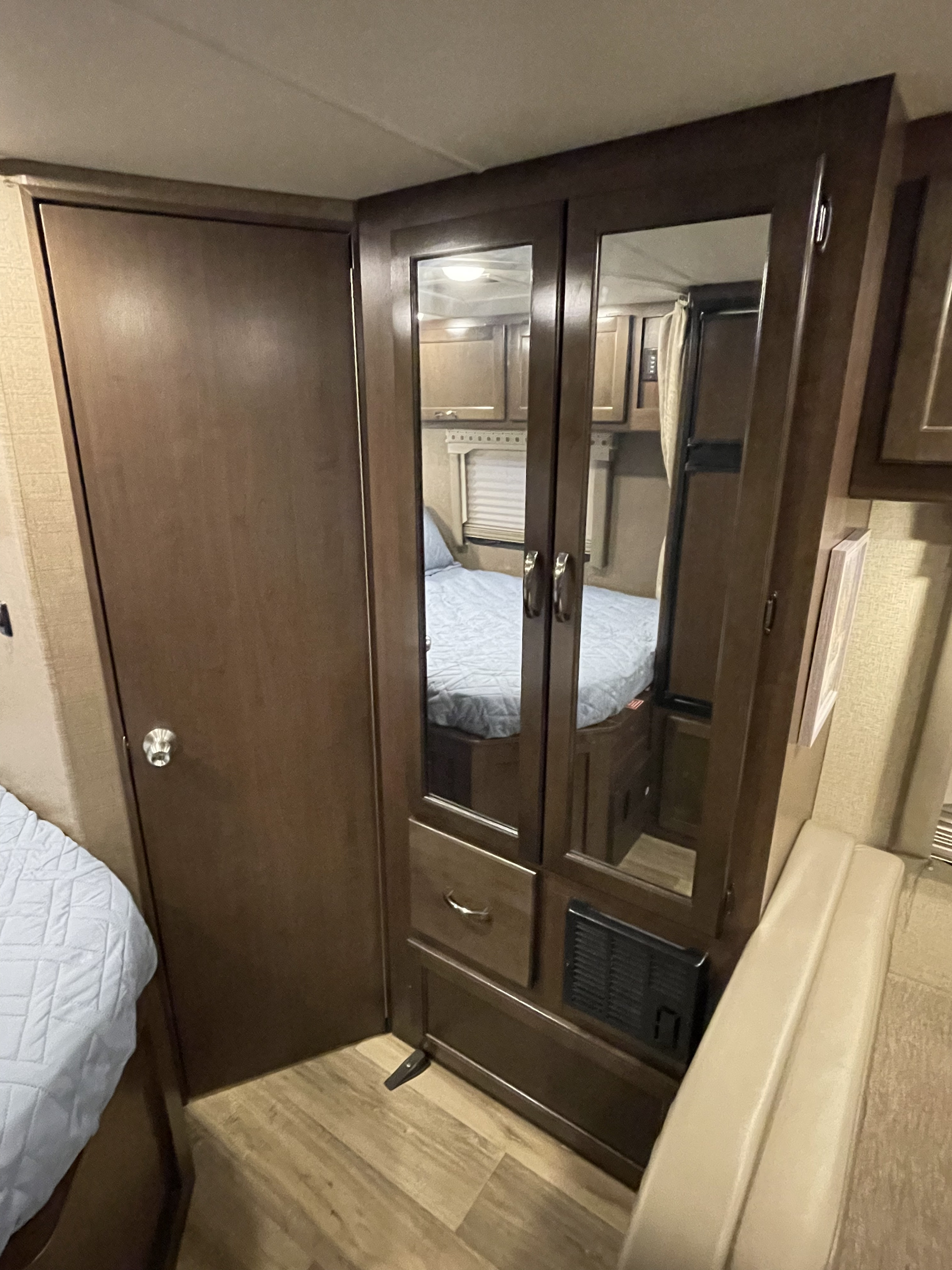Compact RV rental bedroom featuring a mirrored wardrobe, built-in storage, and a connecting wooden door.. Thor Four Winds 2017