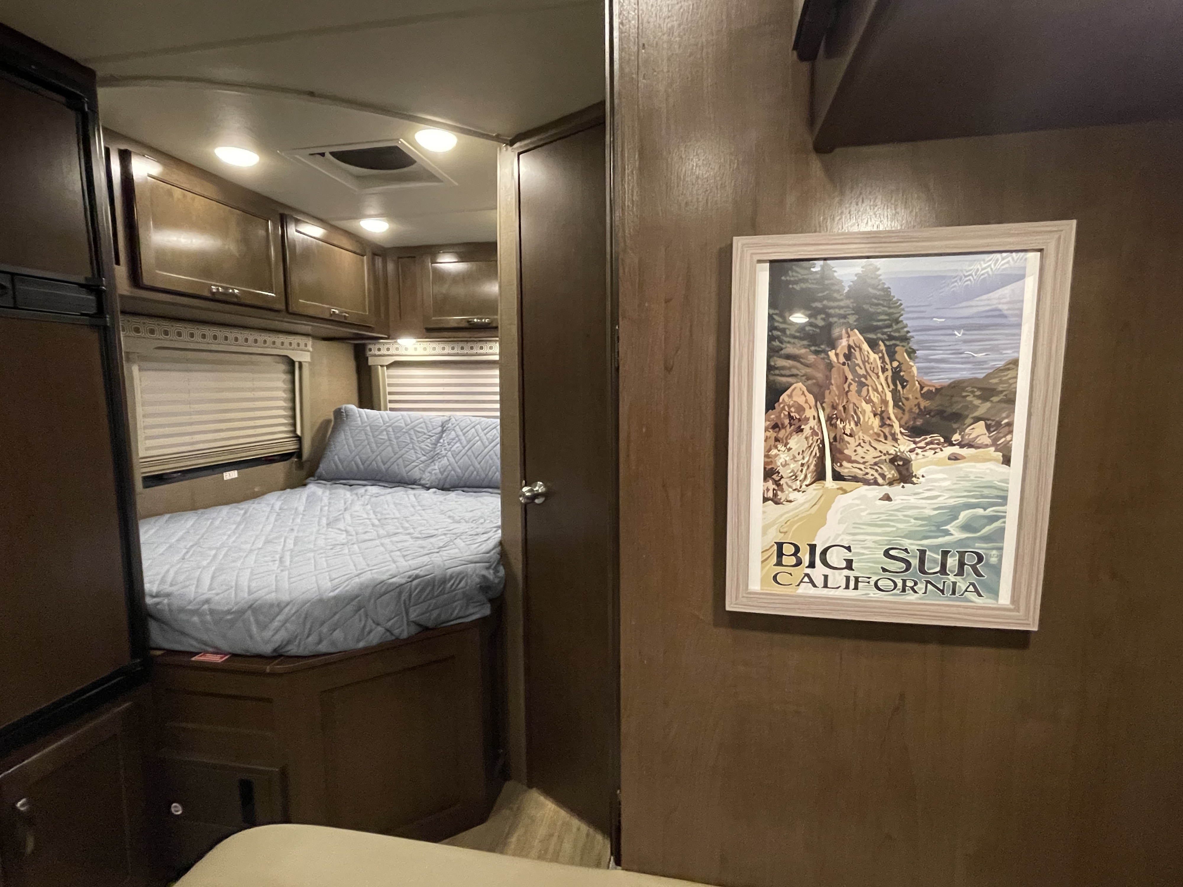 Comfortable RV rental interior with a cozy bed, overhead cabinets, and nature-themed wall art.. Thor Four Winds 2017