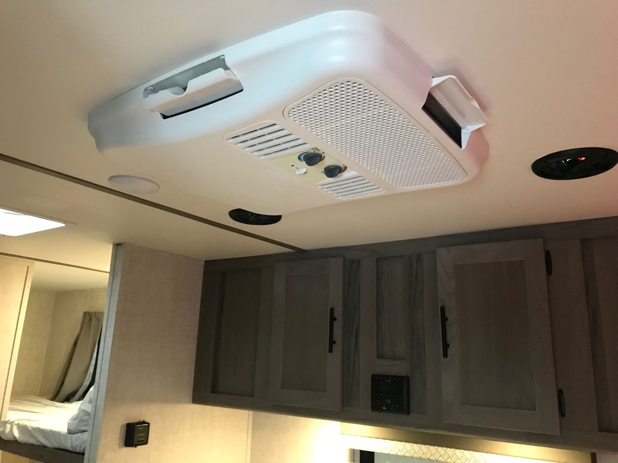 Inside an RV rental: View of a ceiling-mounted AC unit with control knobs, overhead cabinets, and bunk beds.. Gulf Stream Friendship 2022