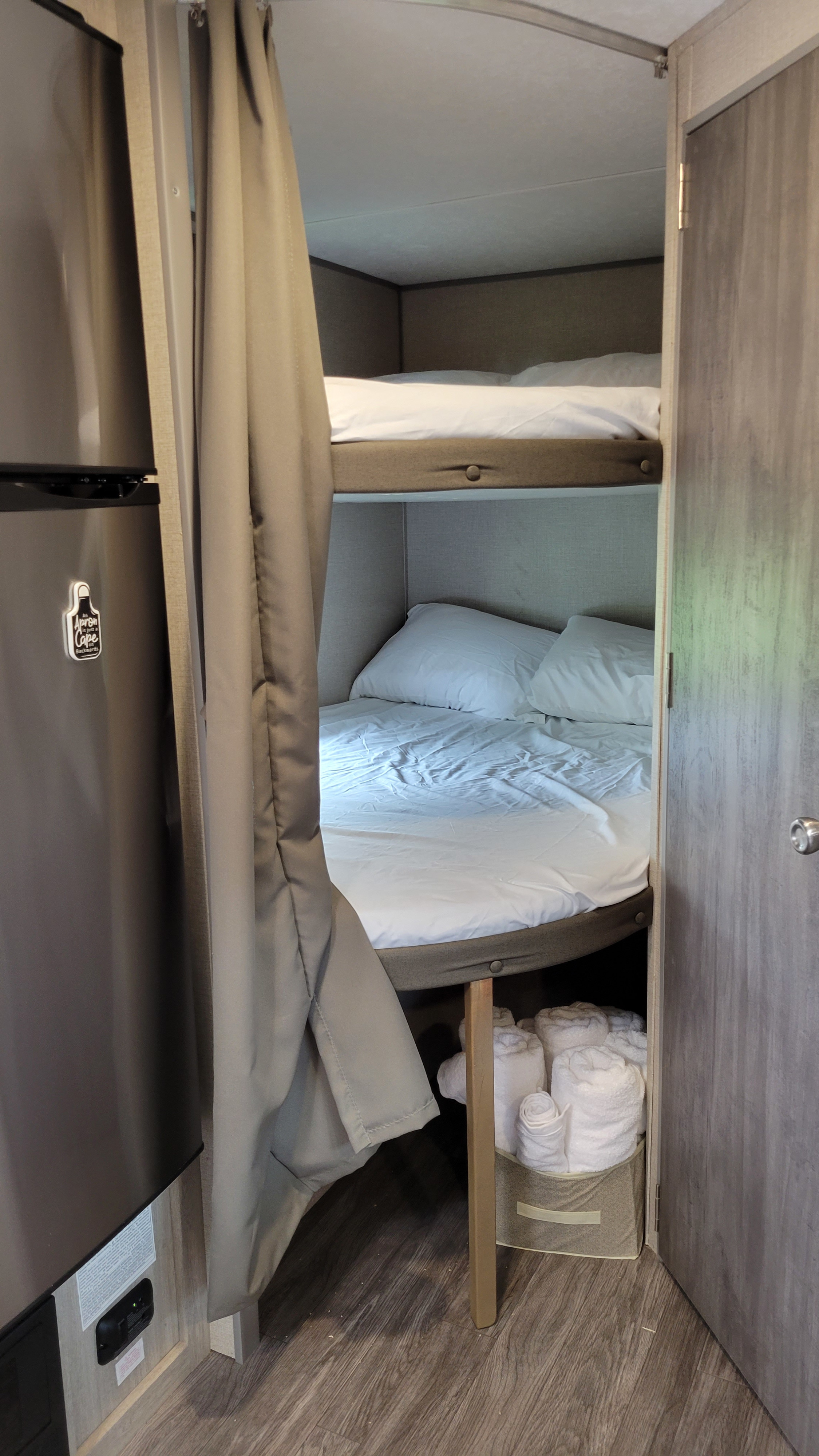 View of an RV rental's bunk bed area, featuring cozy white bedding, a privacy curtain, and a towel bin.. Forest River Coachmen Aurora 2022