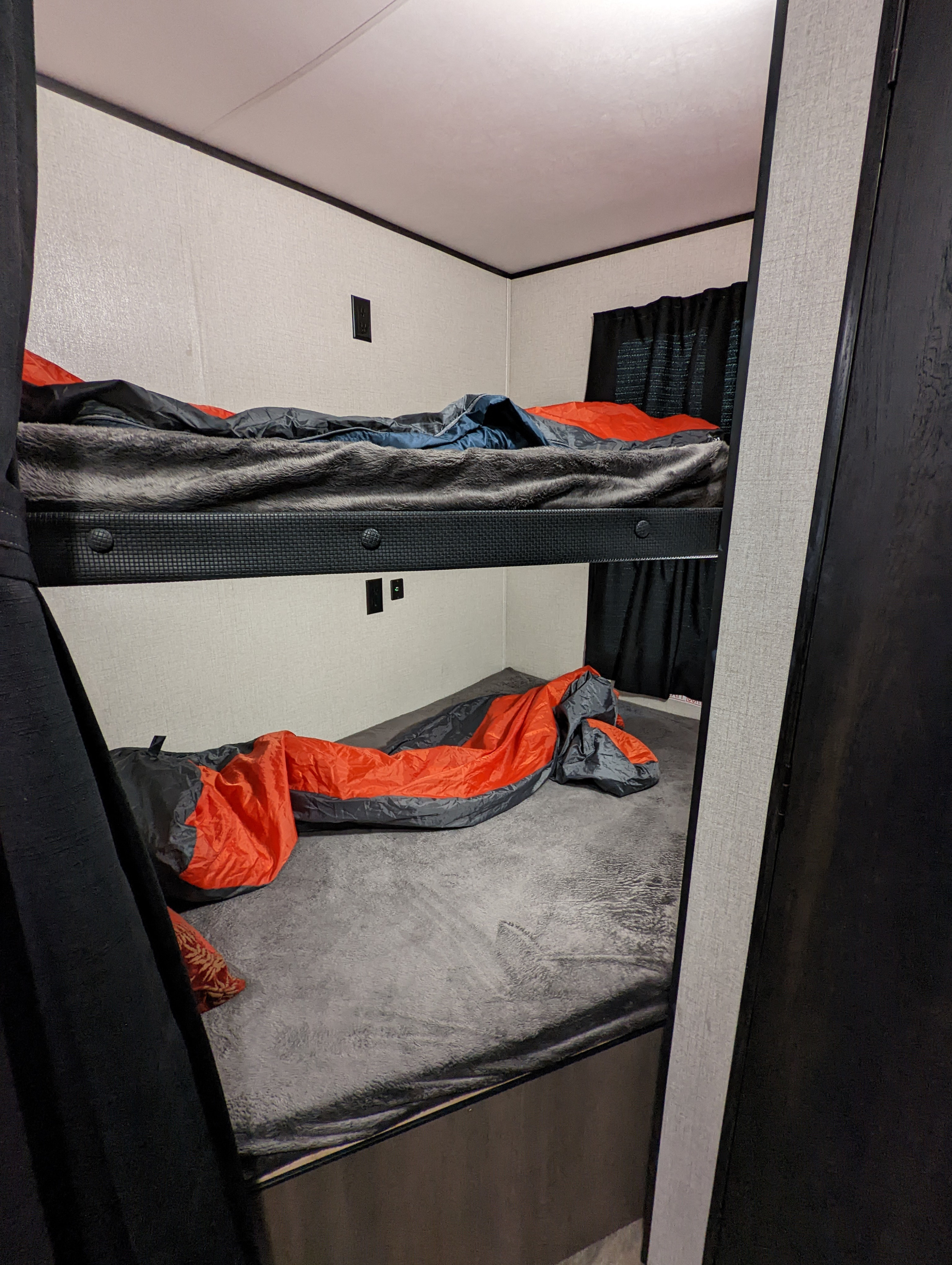 View of an RV rental's compact sleeping area, showing two bunk beds with a grey blanket on the upper and an orange sleeping bag on the lower.. Highland Ridge RV Open Range 2022
