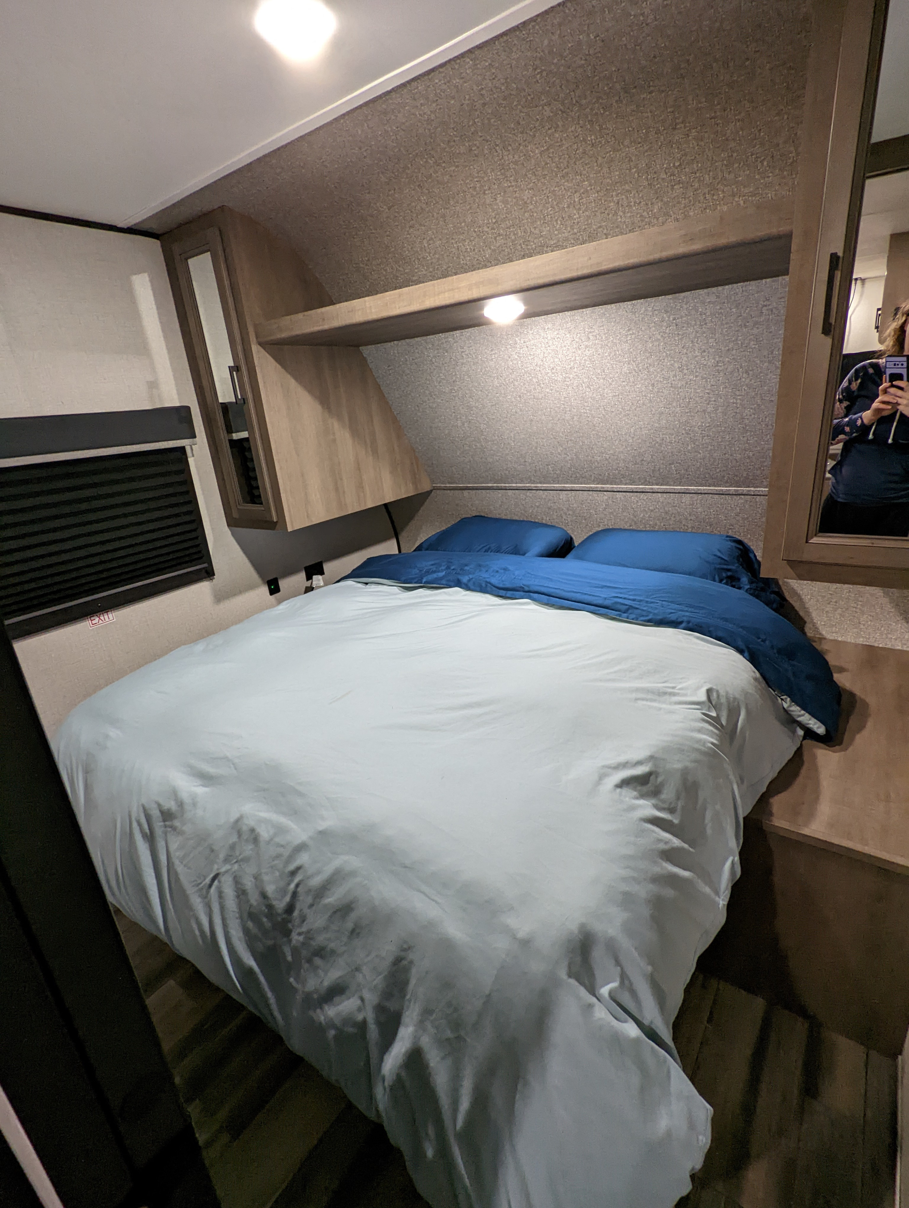 An RV rental bedroom showcasing a bed with blue bedding, overhead cabinets, an emergency exit window, and a mirror.. Highland Ridge RV Open Range 2022