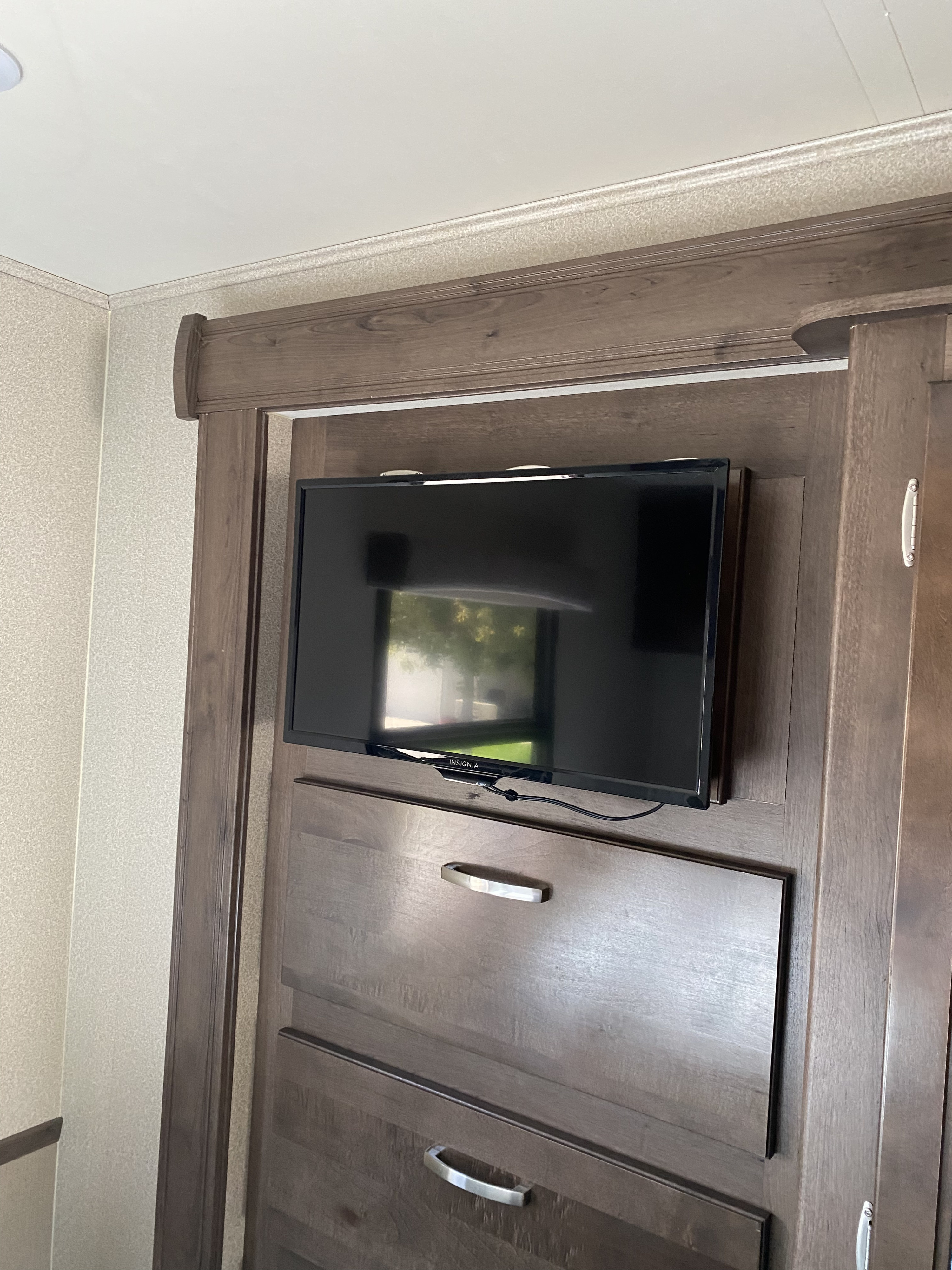 RV rental: A compact entertainment setup with a mounted Insignia TV above functional wooden storage.. Entegra Coach Vision 2020