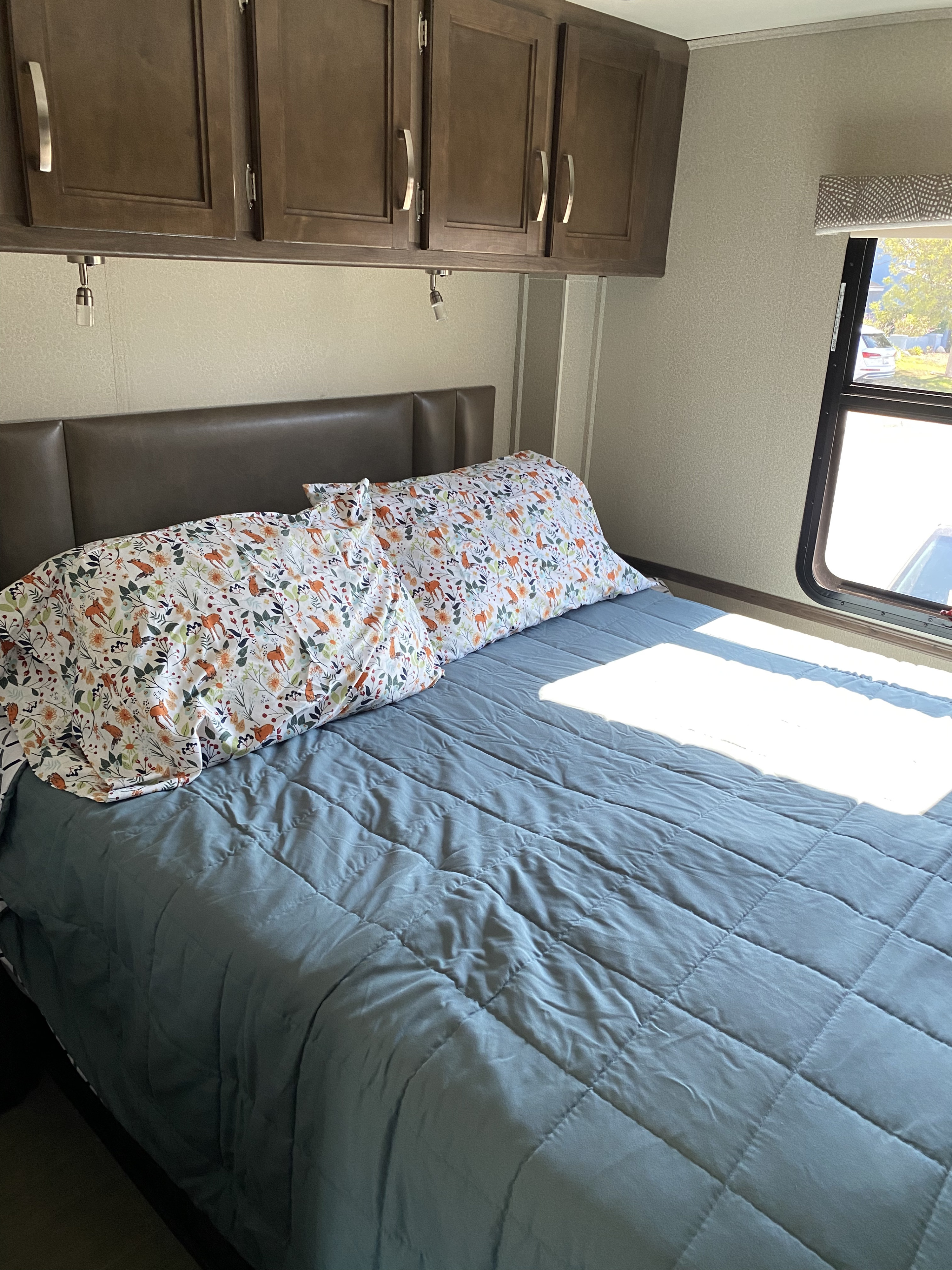 Cozy RV rental bedroom with floral pillows, quilted comforter, and overhead cabinets. Sunlight streams in.. Entegra Coach Vision 2020