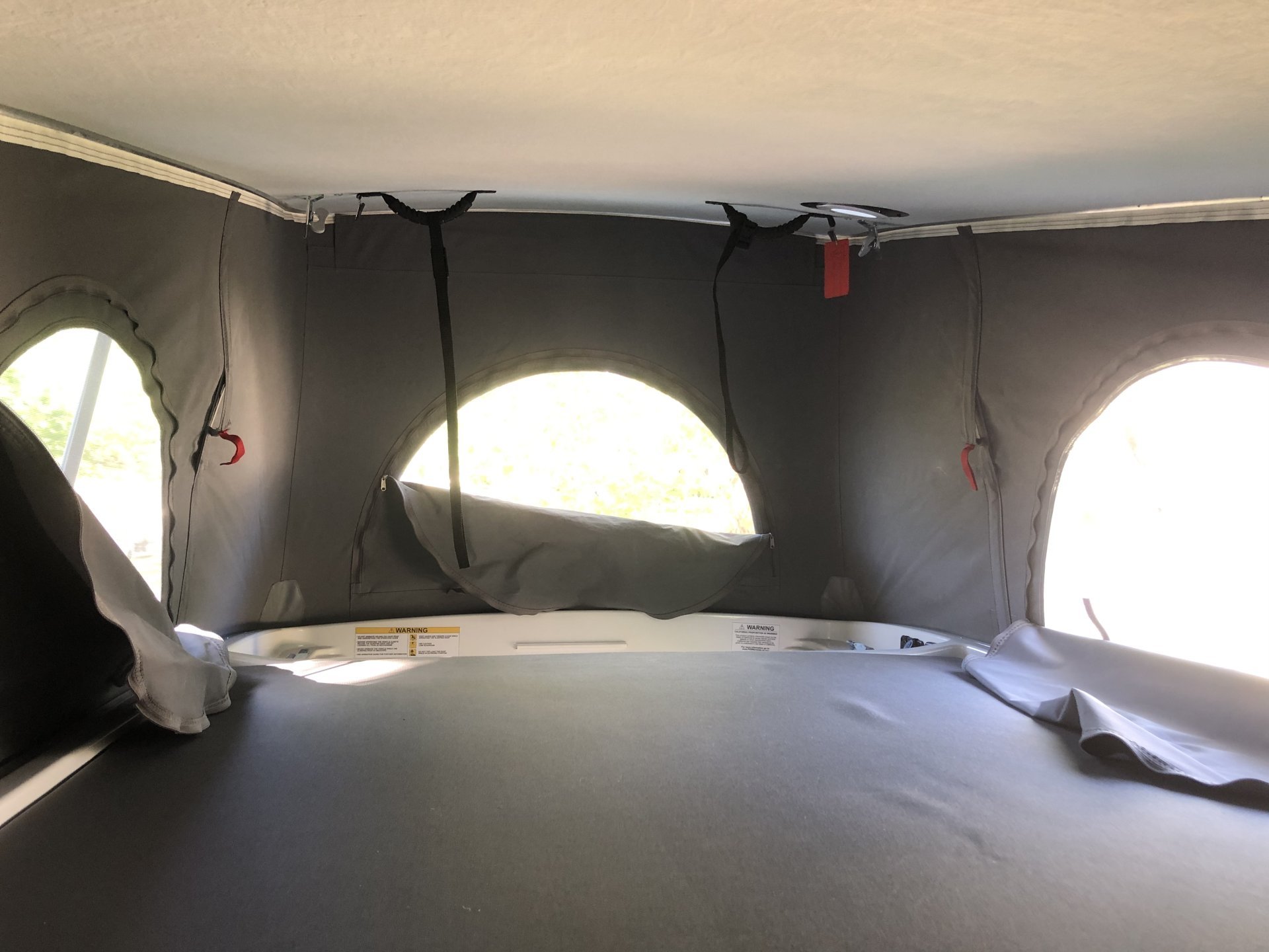 Inside an RV rental pop-top, showing a flat bed, gray fabric walls with open round windows, and ceiling straps.. Winnebago Solis 2022