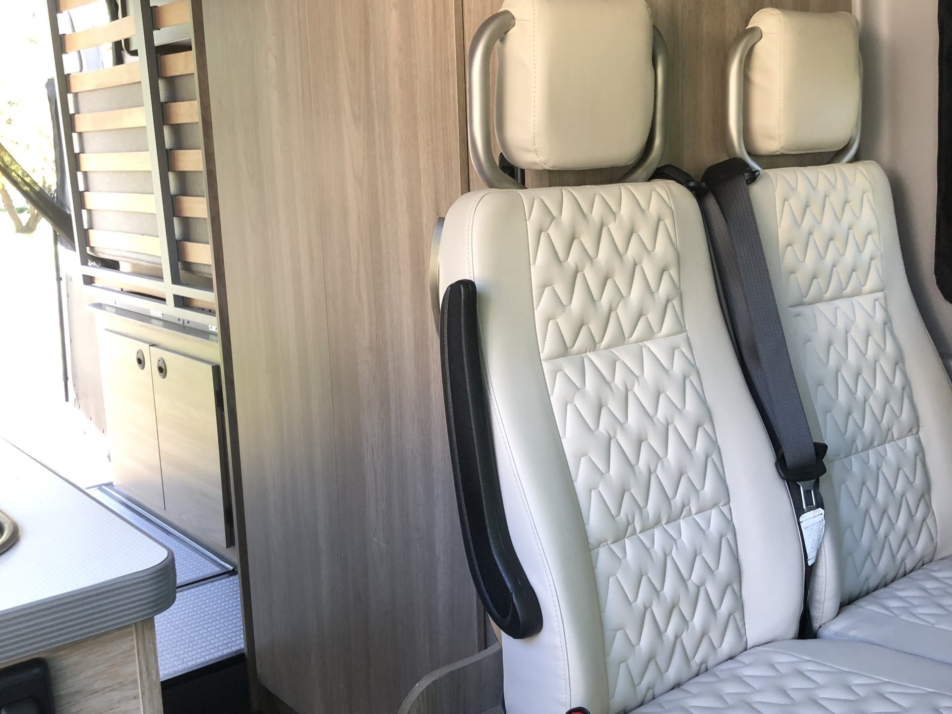 View inside an RV rental showing modern white quilted seats, wooden cabinets, and versatile sleeping/storage solutions.. Winnebago Solis 2022