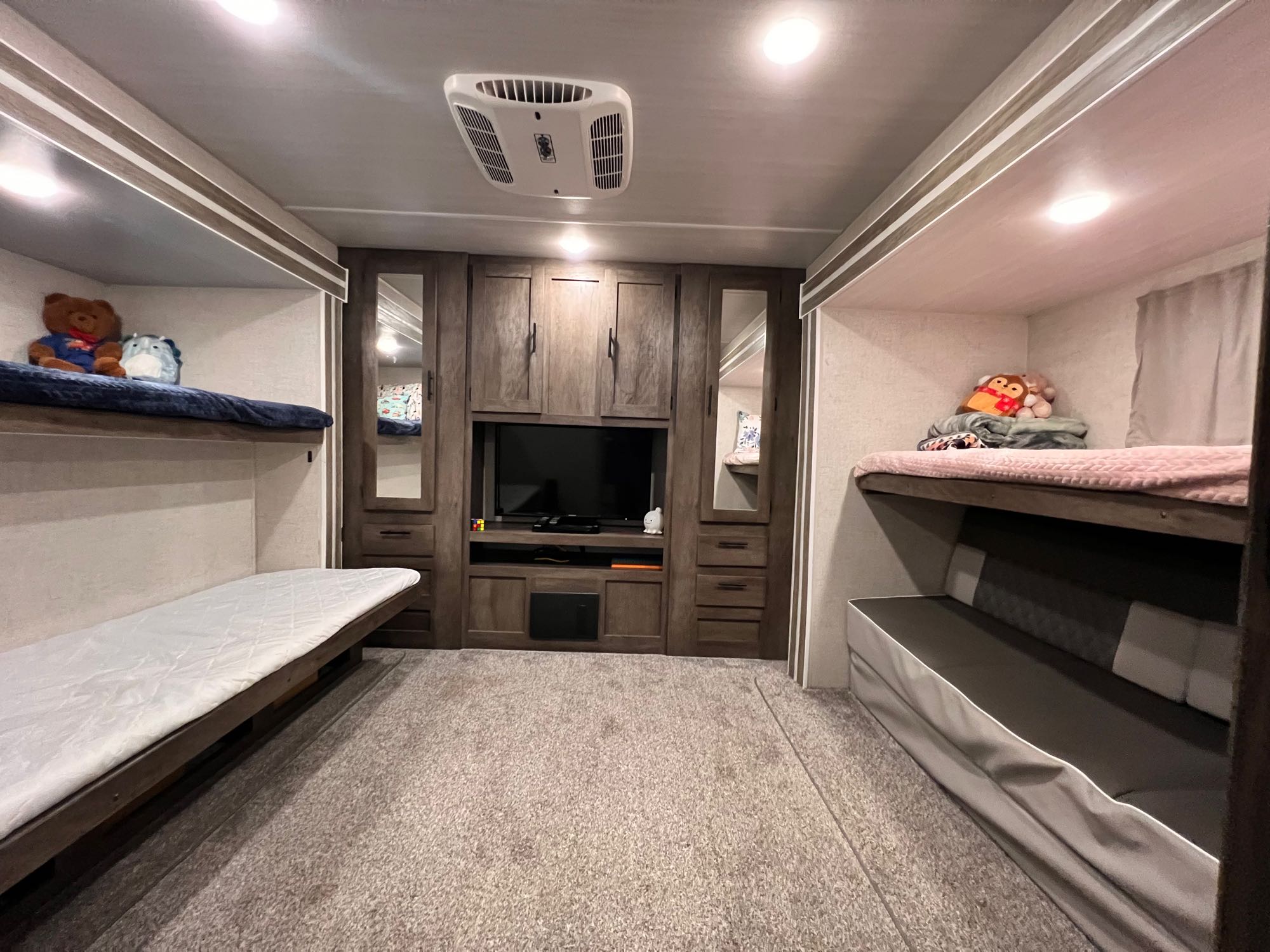 This RV rental offers a cozy interior with bunk beds on both sides, a central TV unit, and soft carpet flooring.. Forest River Wildwood 2021