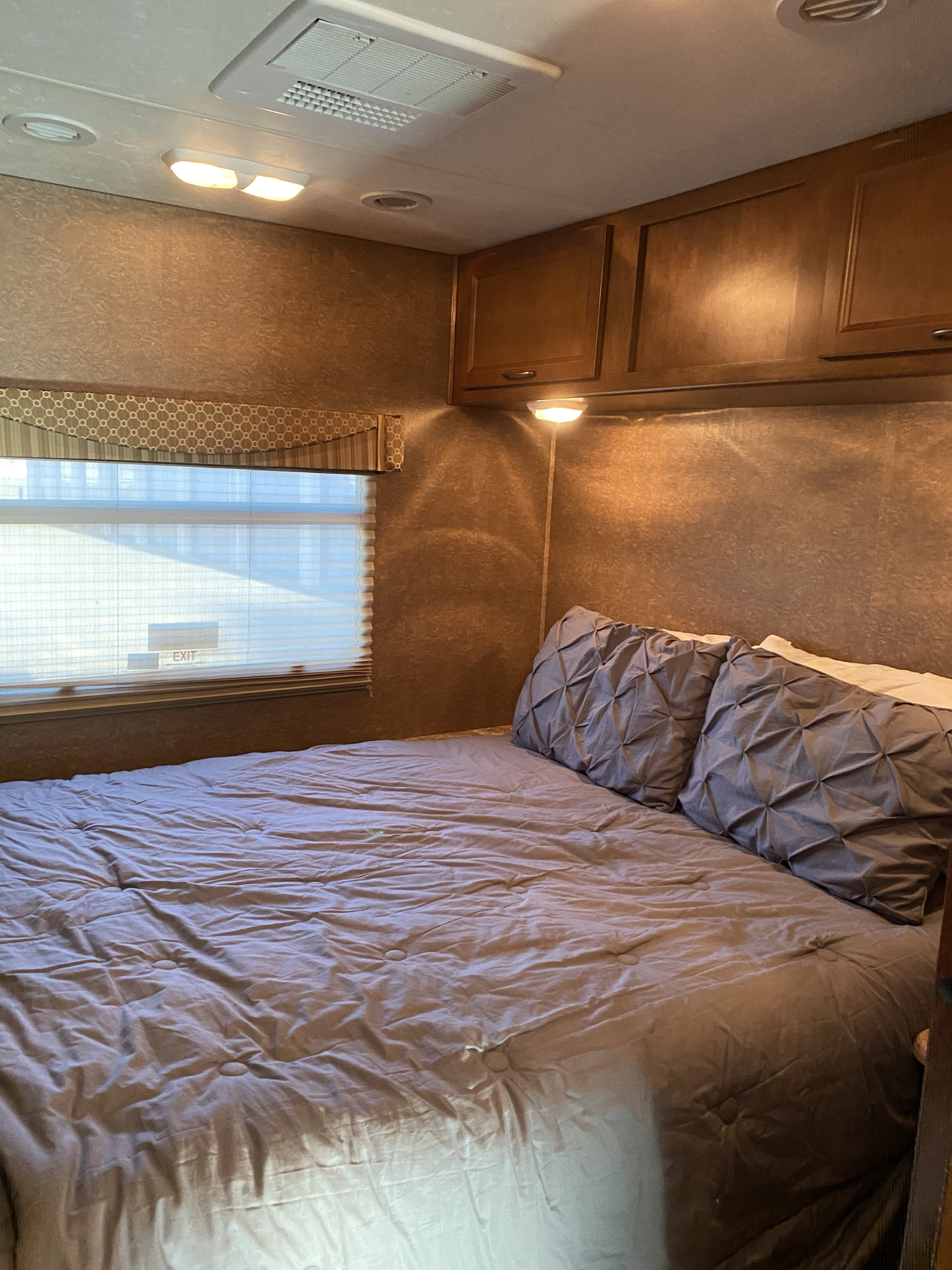 Comfortable RV rental bedroom featuring a grey bed, window with blinds, and overhead cabinets. A cozy travel retreat.. Forest River Coachmen Pursuit 2015