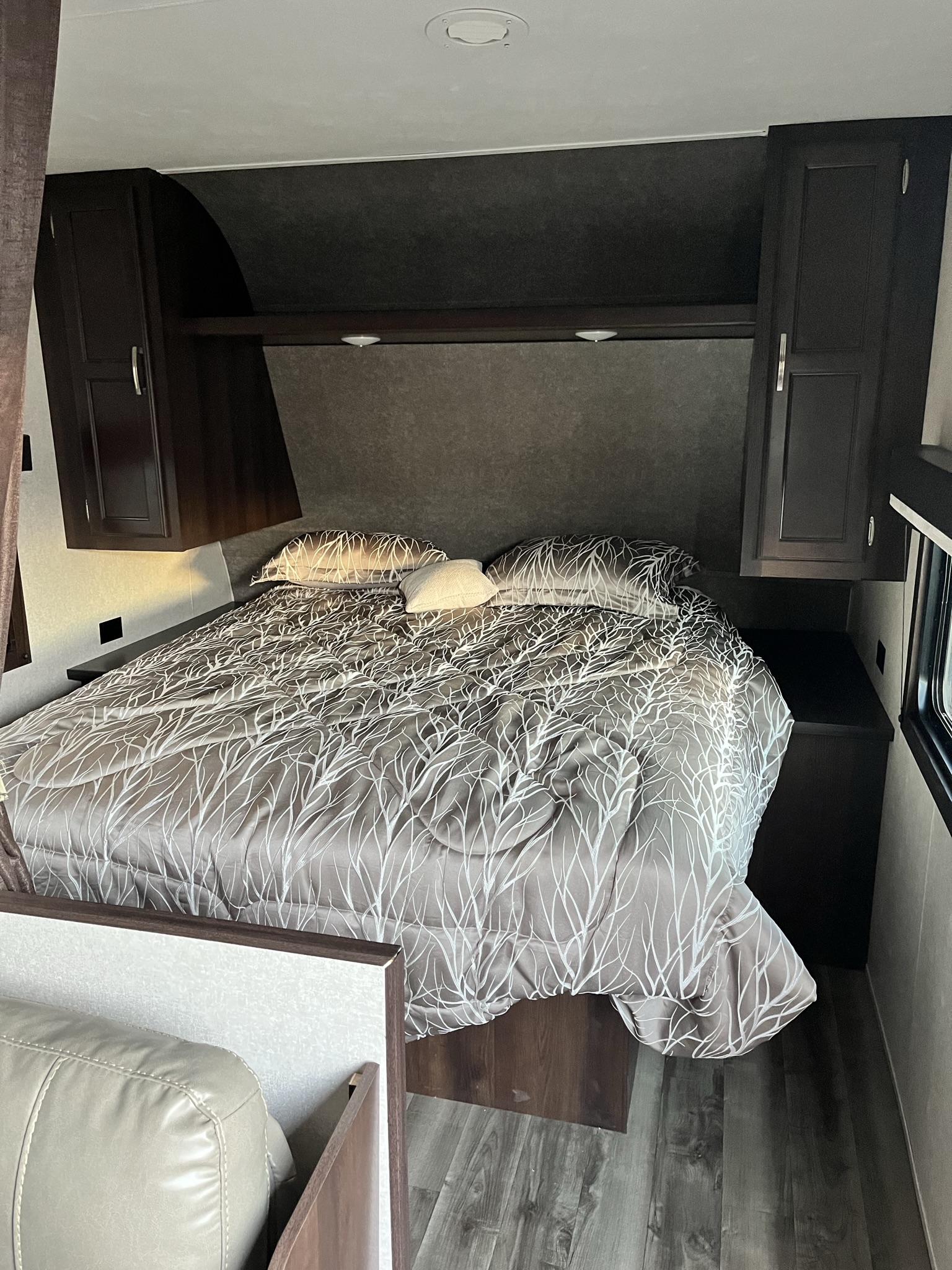 Inside this cozy RV rental, discover a compact bedroom with a patterned bed, overhead cabinets, and dark wood trim.. Jayco Jay Flight SLX Rocky Mountain Edition 2020