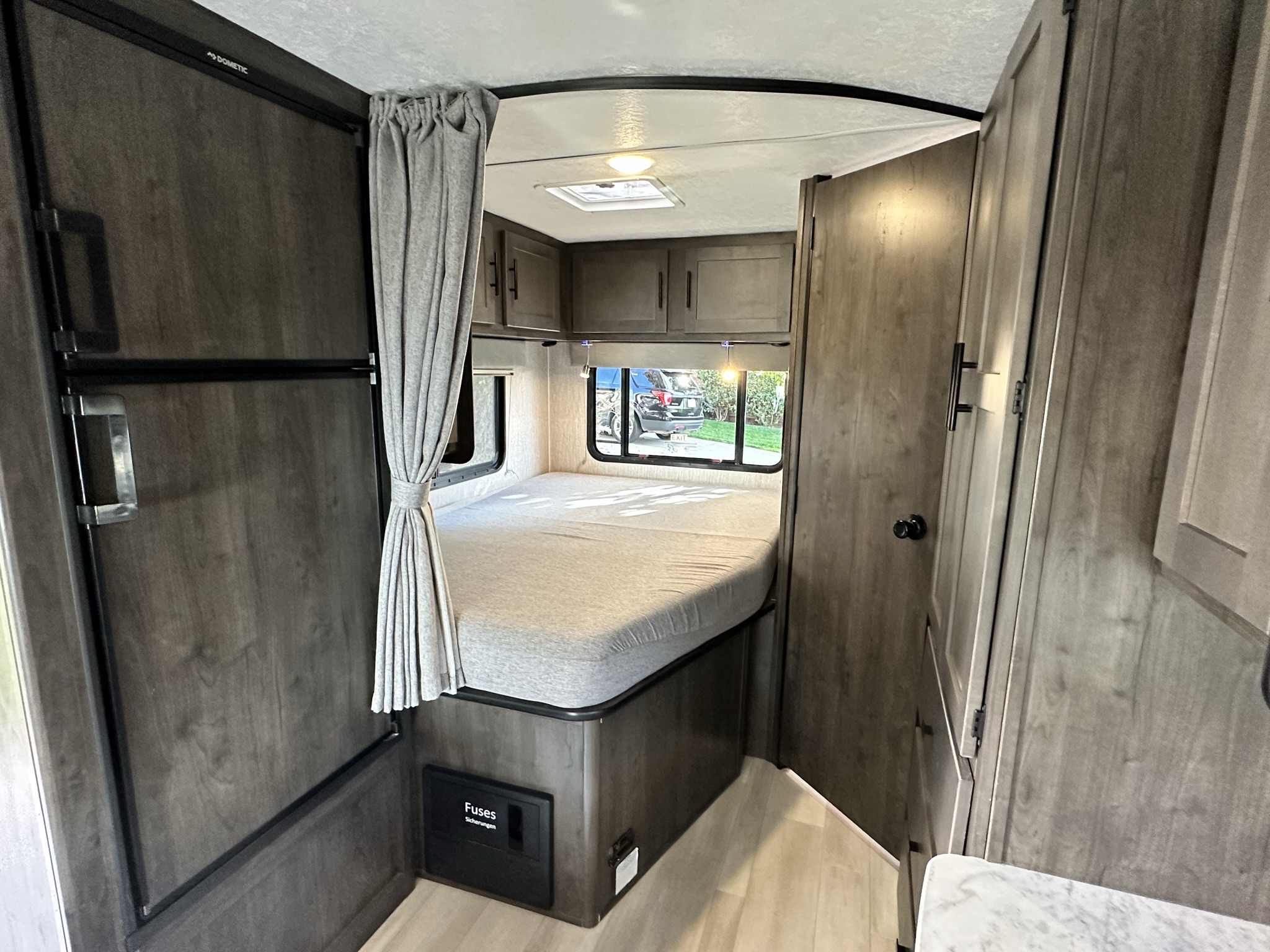 Spacious RV rental bedroom featuring a comfortable bed, overhead cabinets, a Dometic fridge, and modern wood tones.. Coachmen Leprechaun 2022