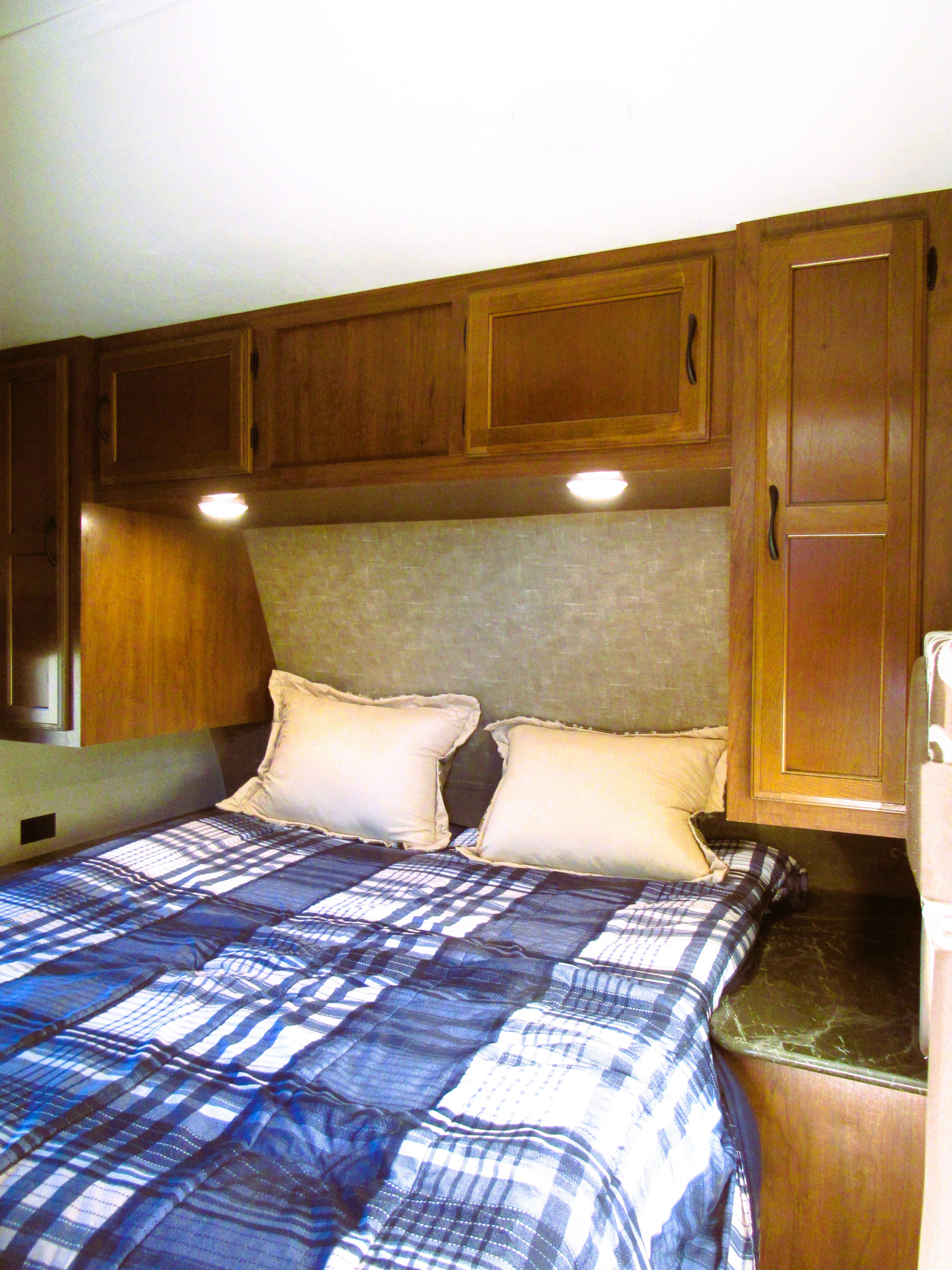 This rv rental bedroom features a comfortable bed with blue plaid bedding, pillows, and ample wooden storage.. Jayco Jay Flight 2016