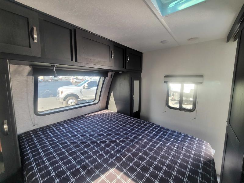 Cozy RV rental bedroom features a plaid bed, ample dark cabinets, and bright windows, showcasing the spacious interior.. Coachmen 257BHS 2022