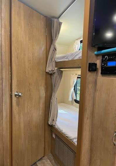 Cozy bunk beds with privacy curtains and an entertainment system in this RV rental's interior, perfect for comfortable sleeping.. Gulf Stream Vintage Cruiser 2022