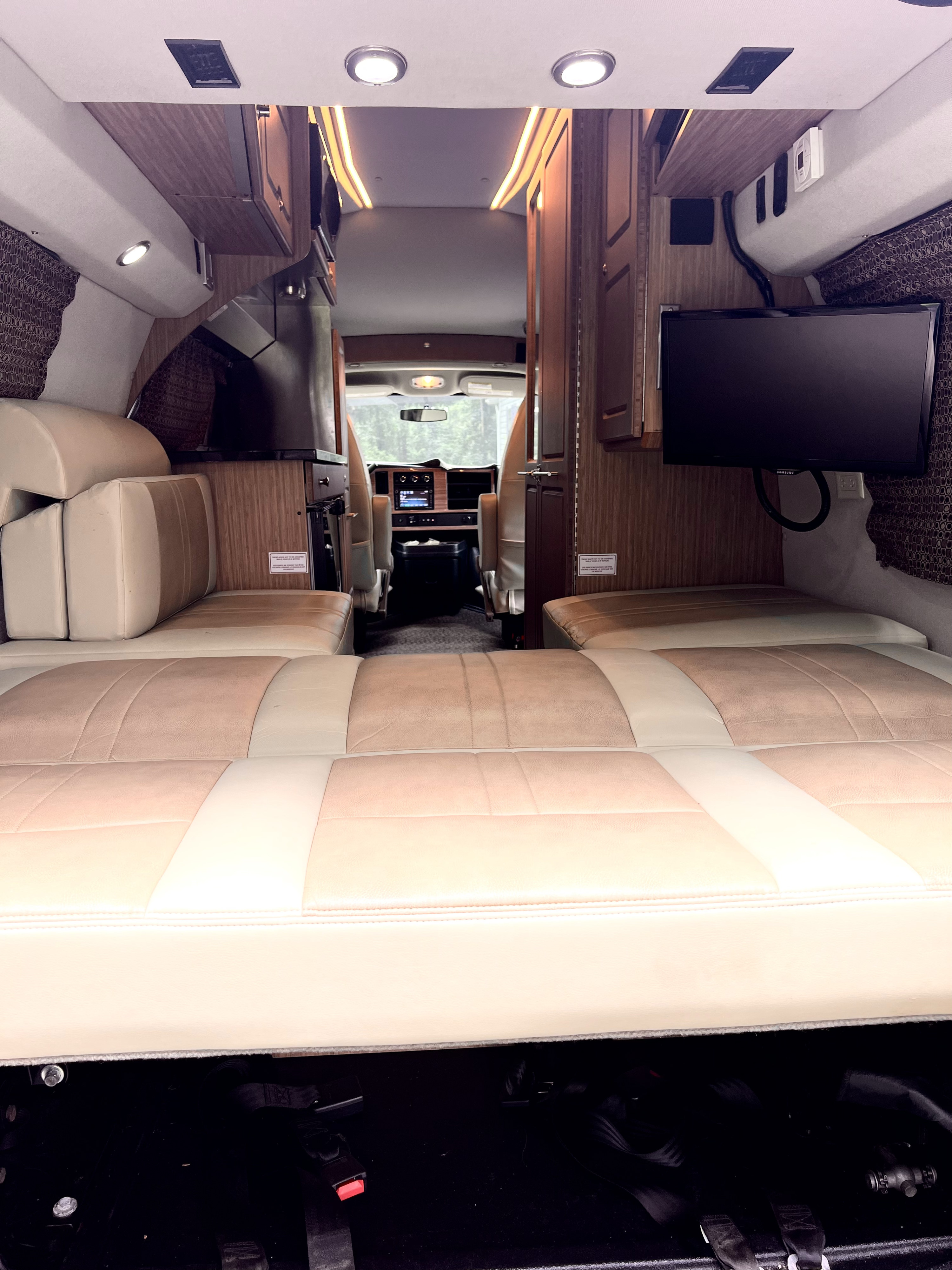 Bright RV rental interior, showing plush convertible bed/seating, mounted TV, and front cabin view.. Roadtrek Roadtrek Class B 2015